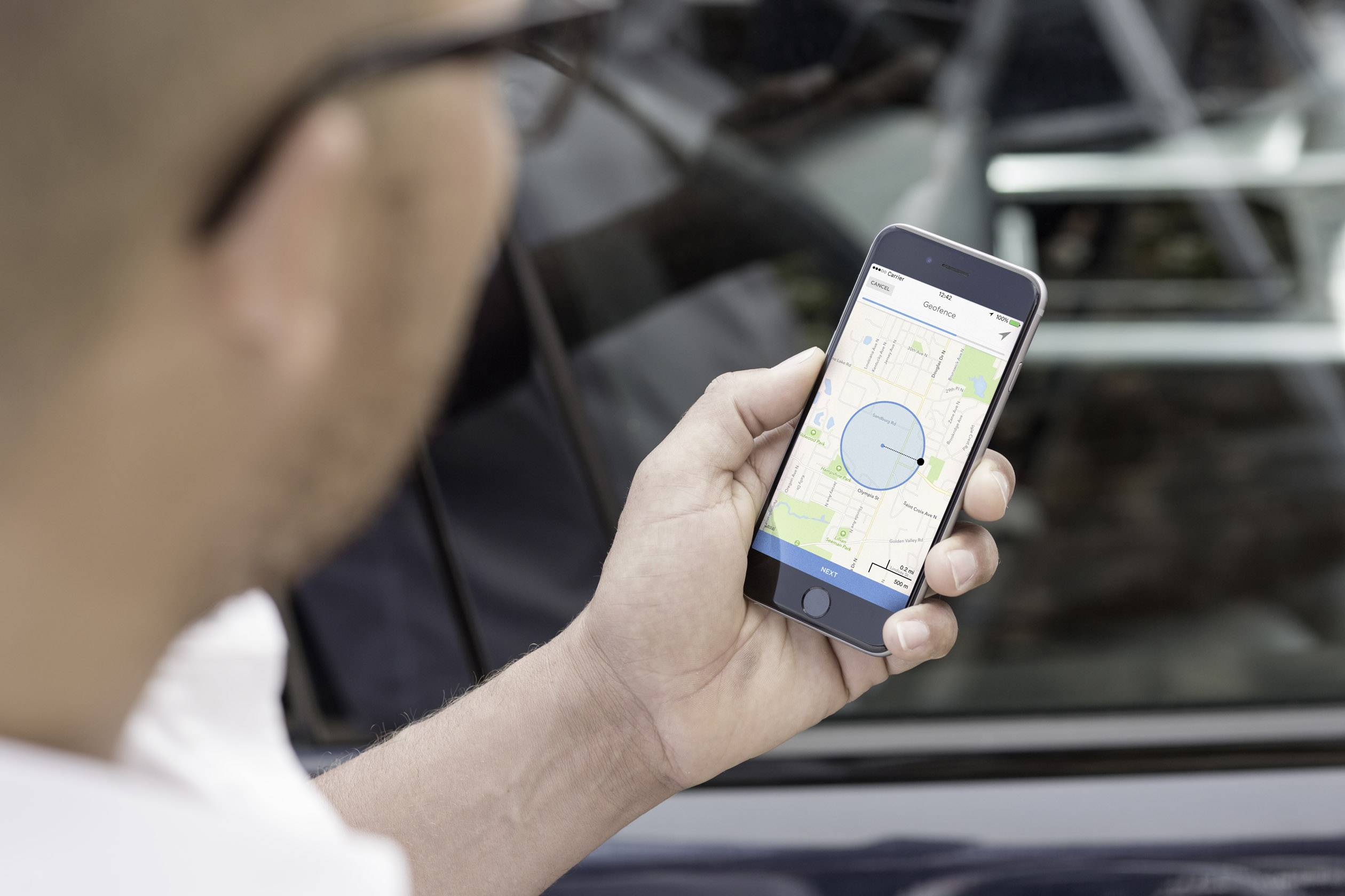 Person hält ein Smartphone mit einer geöffneten Karten-App, Fokus auf blauen Kreis als Standortanzeige. Hintergrund zeigt verschwommenes Auto.