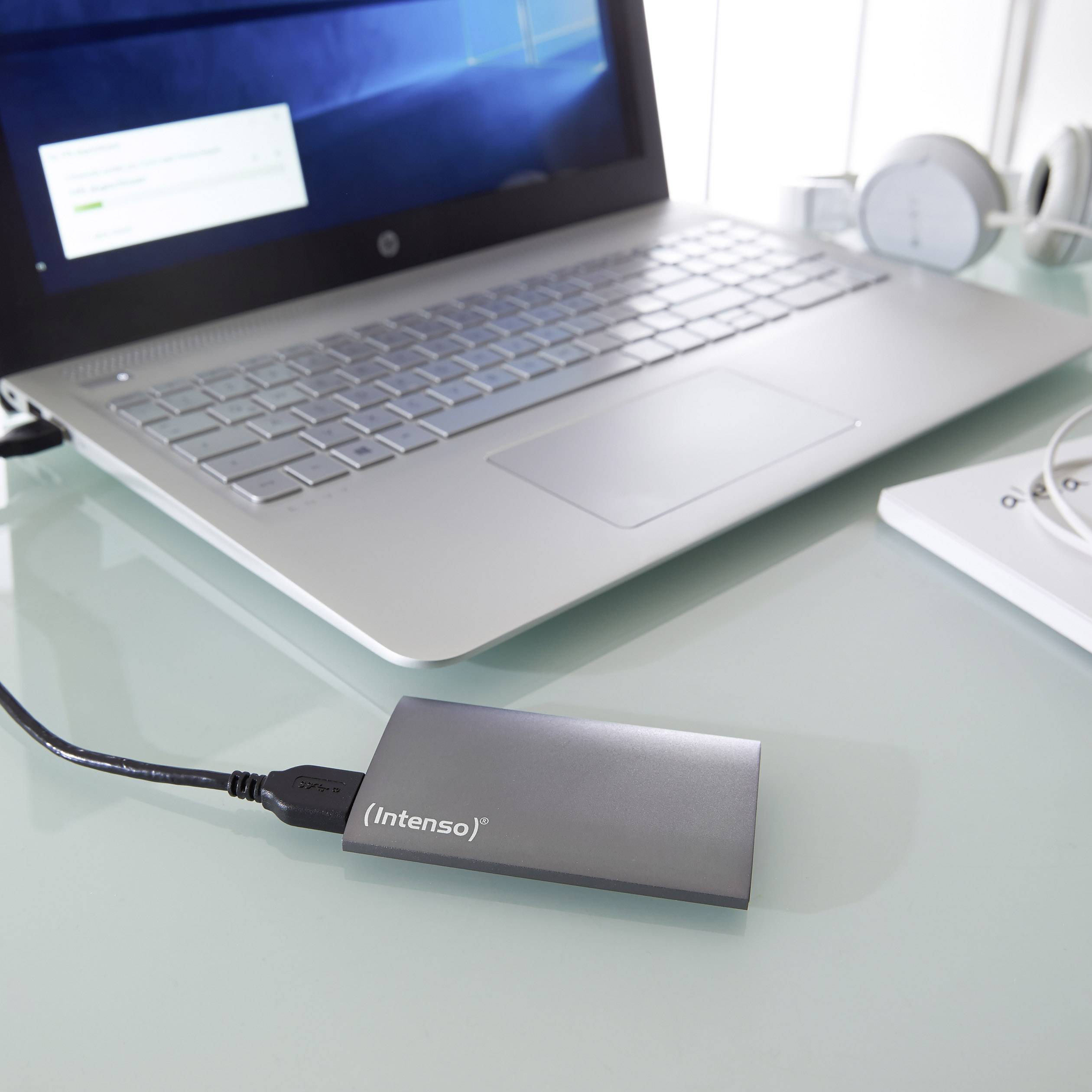 Externe Festplatte 'Intenso' verbunden mit einem Laptop auf einem Schreibtisch, symbolisiert Datenübertragung oder Datensicherung.