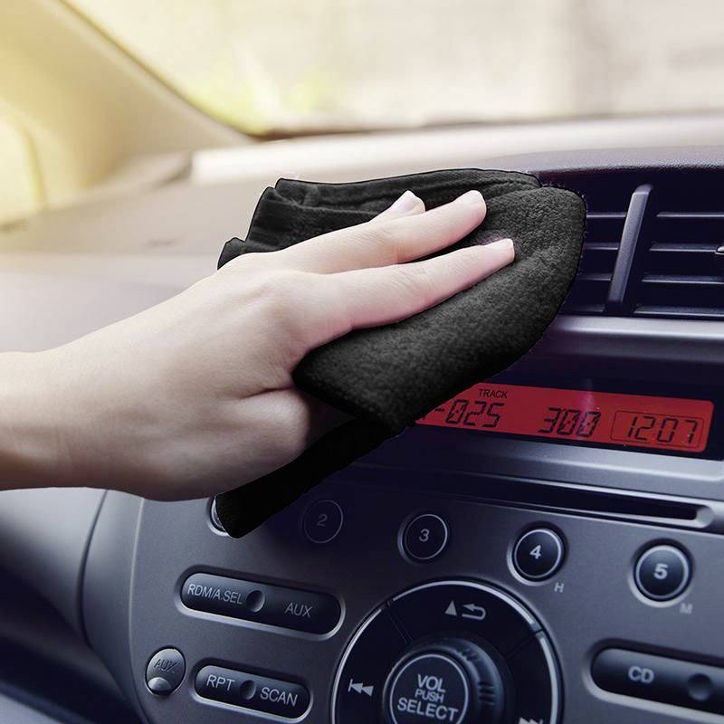 Hand wischt das Armaturenbrett eines Autos mit einem Tuch ab, während die Autoanzeige die Uhrzeit anzeigt.