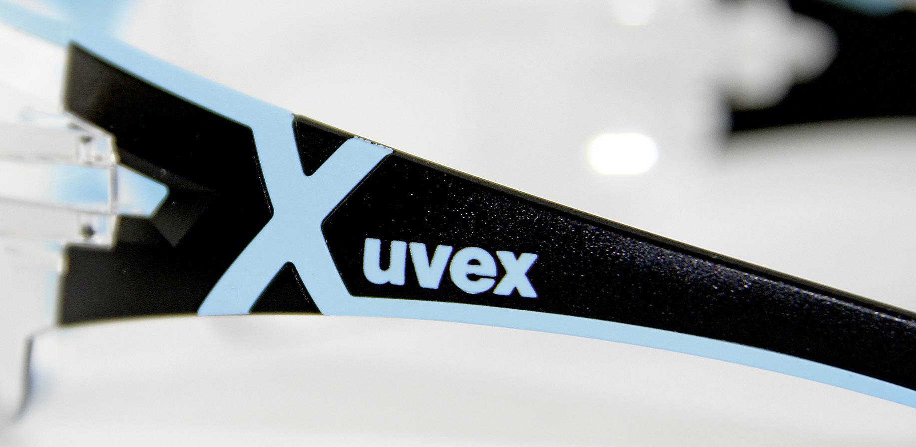 Nahaufnahme eines Brillenbügels mit dem Markennamen 'uvex' und einem großen, blauen 'X'. Der Bügel hat eine schwarze und blaue Farbgebung.