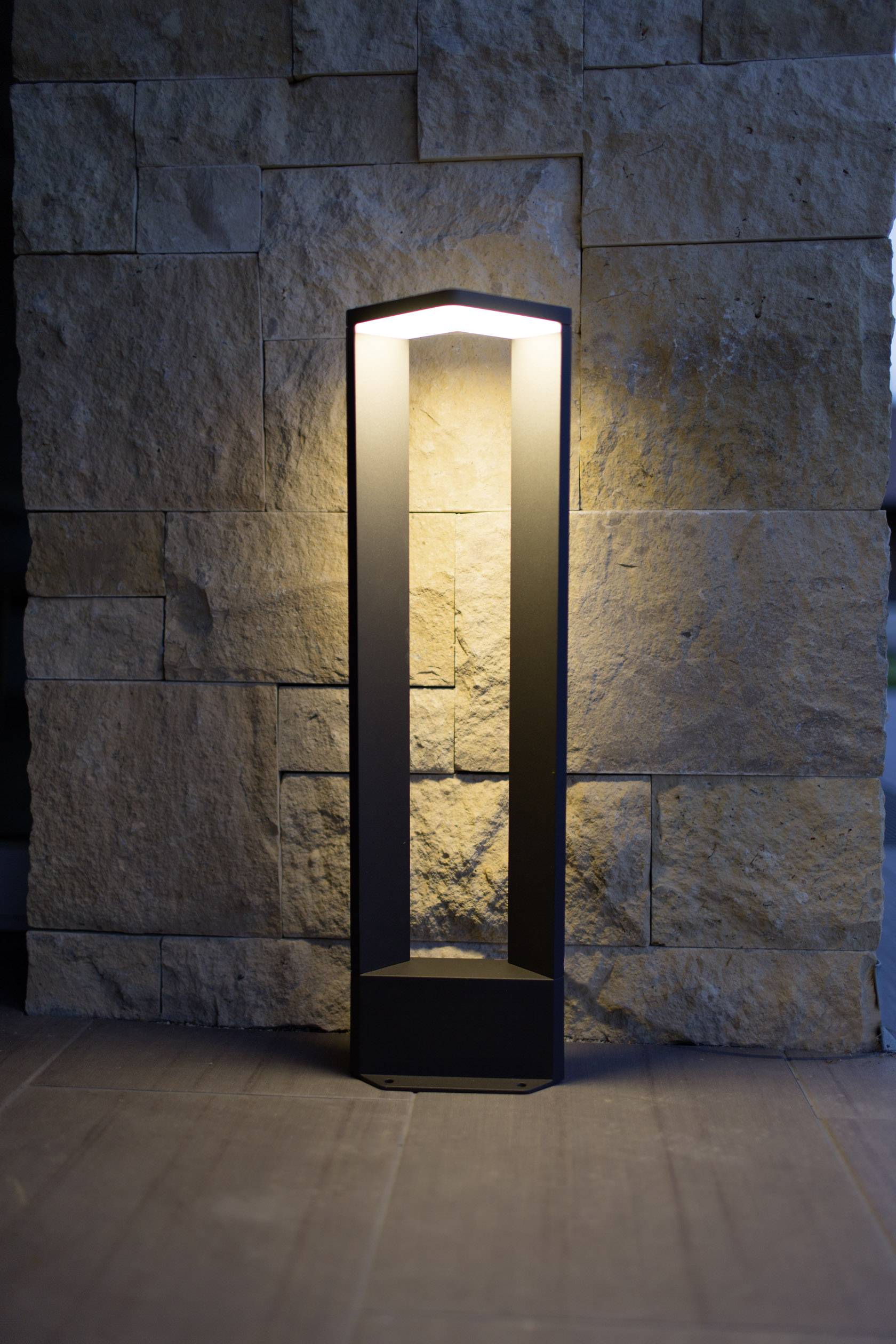 Eine moderne schwarze Stehlampe beleuchtet eine Wand aus grobem Naturstein, schafft eine warme und einladende Atmosphäre.