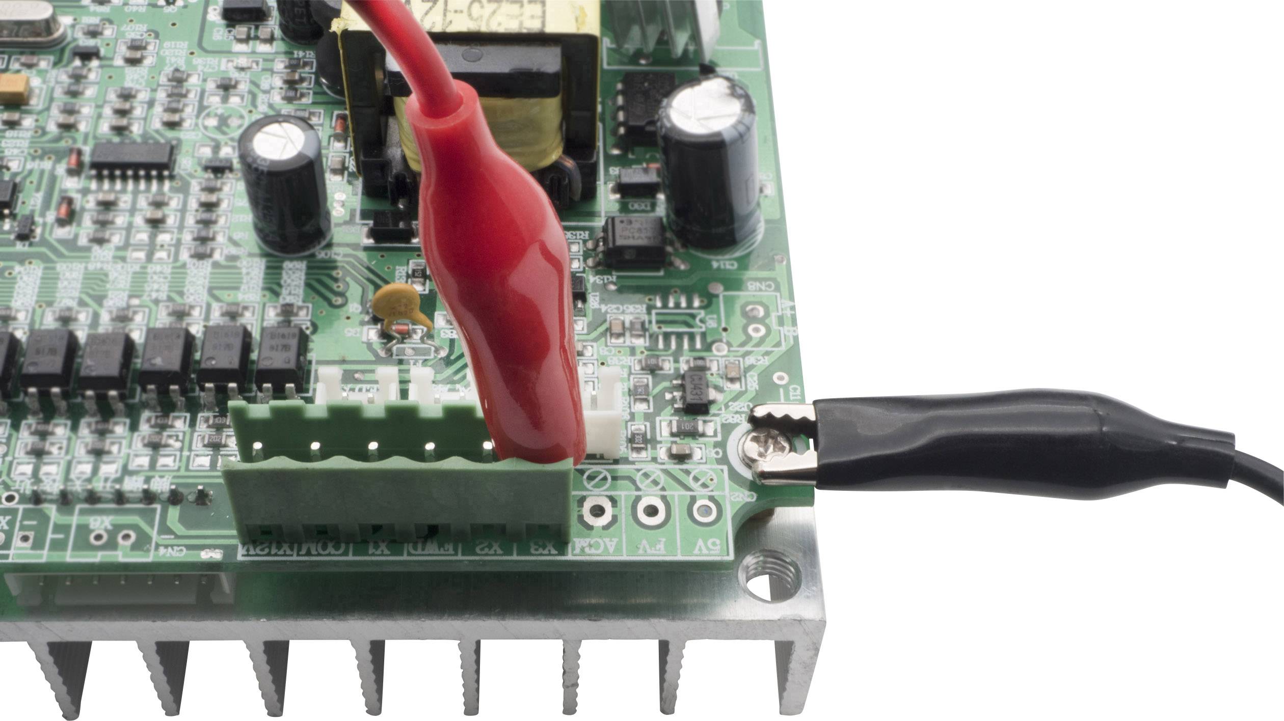 Eine elektronische Leiterplatte mit Komponenten, an die zwei Krokodilklemmen angeschlossen sind, eine rote und eine schwarze.