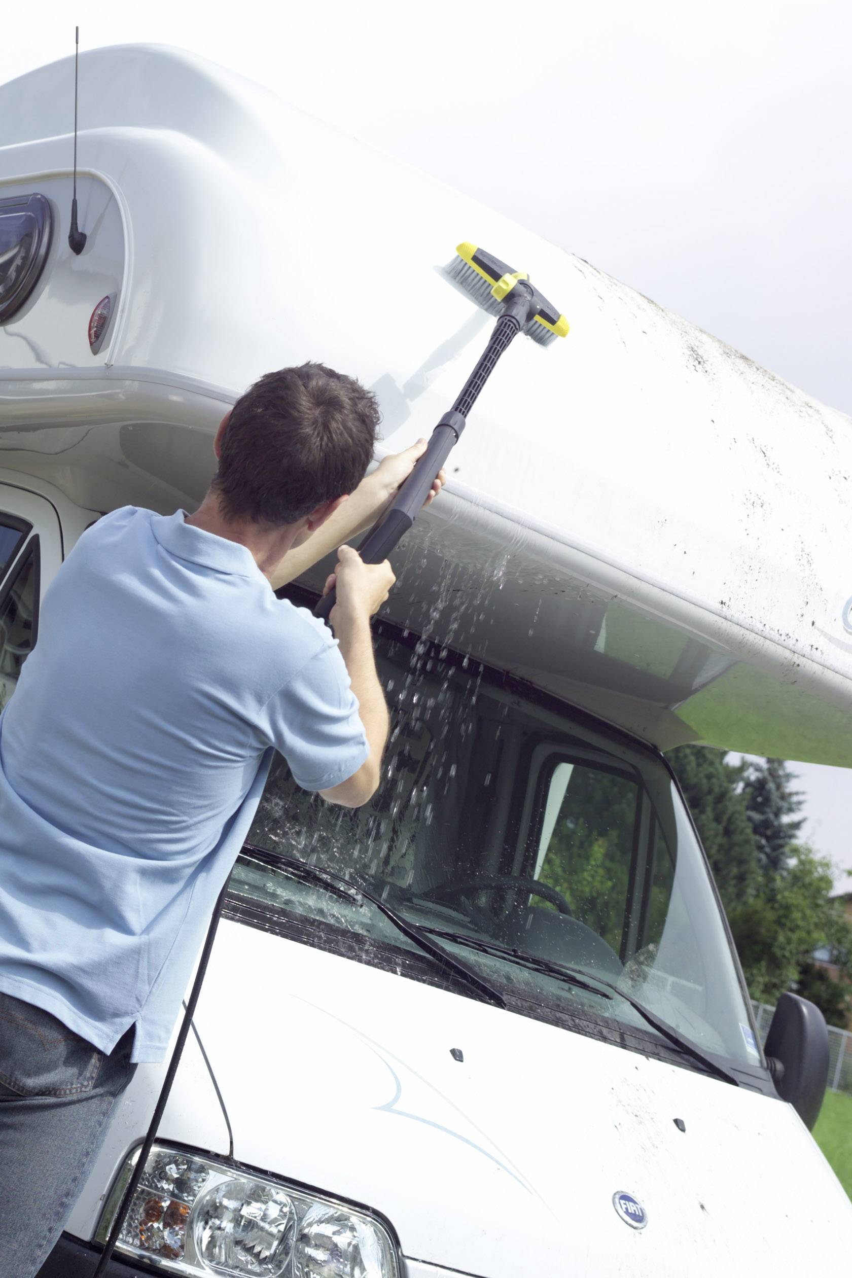 Eine Person reinigt das Dach eines Wohnmobils mit einem Hochdruckreiniger. Wasser spritzt, während Schmutz entfernt wird.