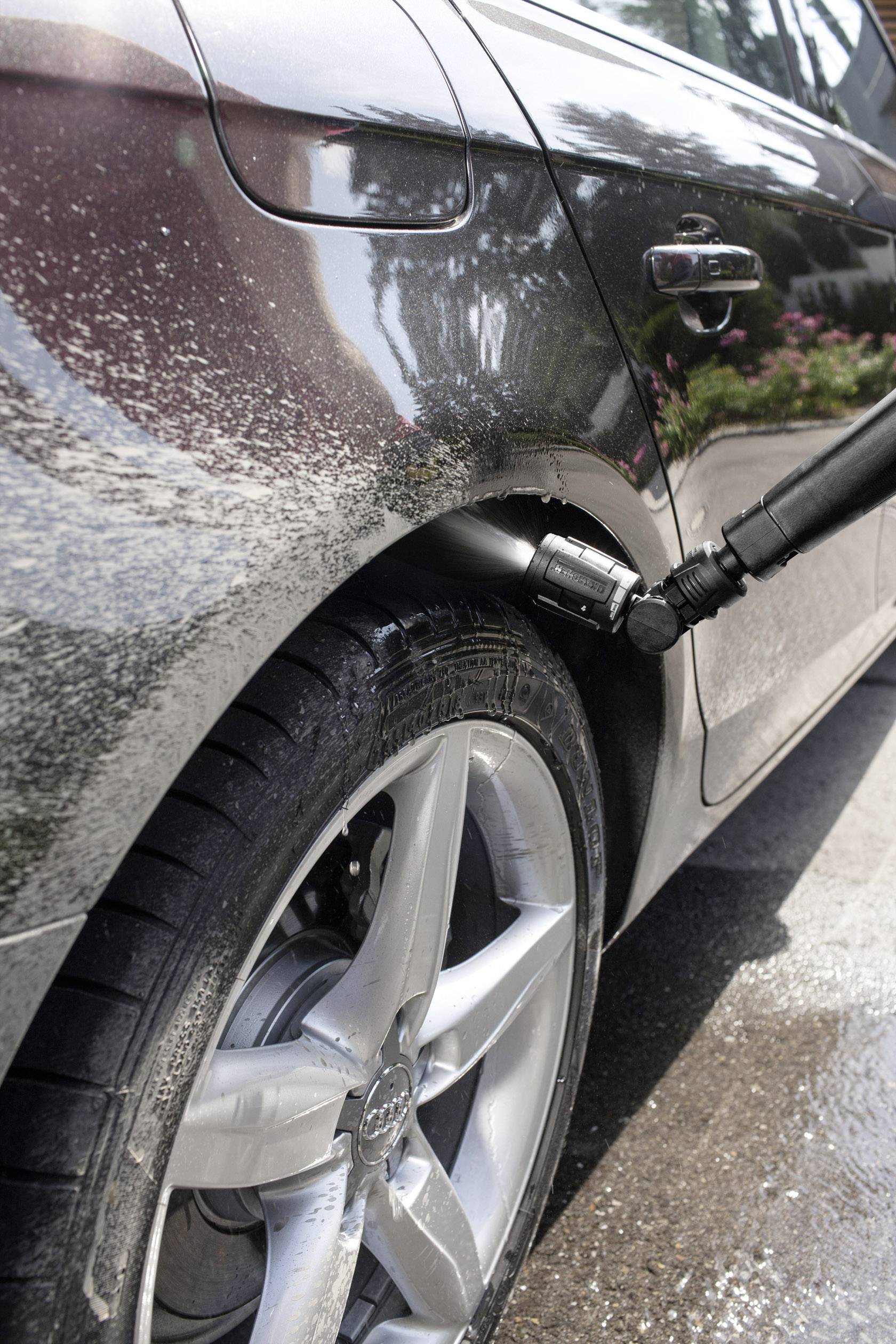 Auto wird mit Hochdruckreiniger am Rad sauber gemacht. Wassertropfen und Schaum sind auf dem Reifen und der Karosserie sichtbar.