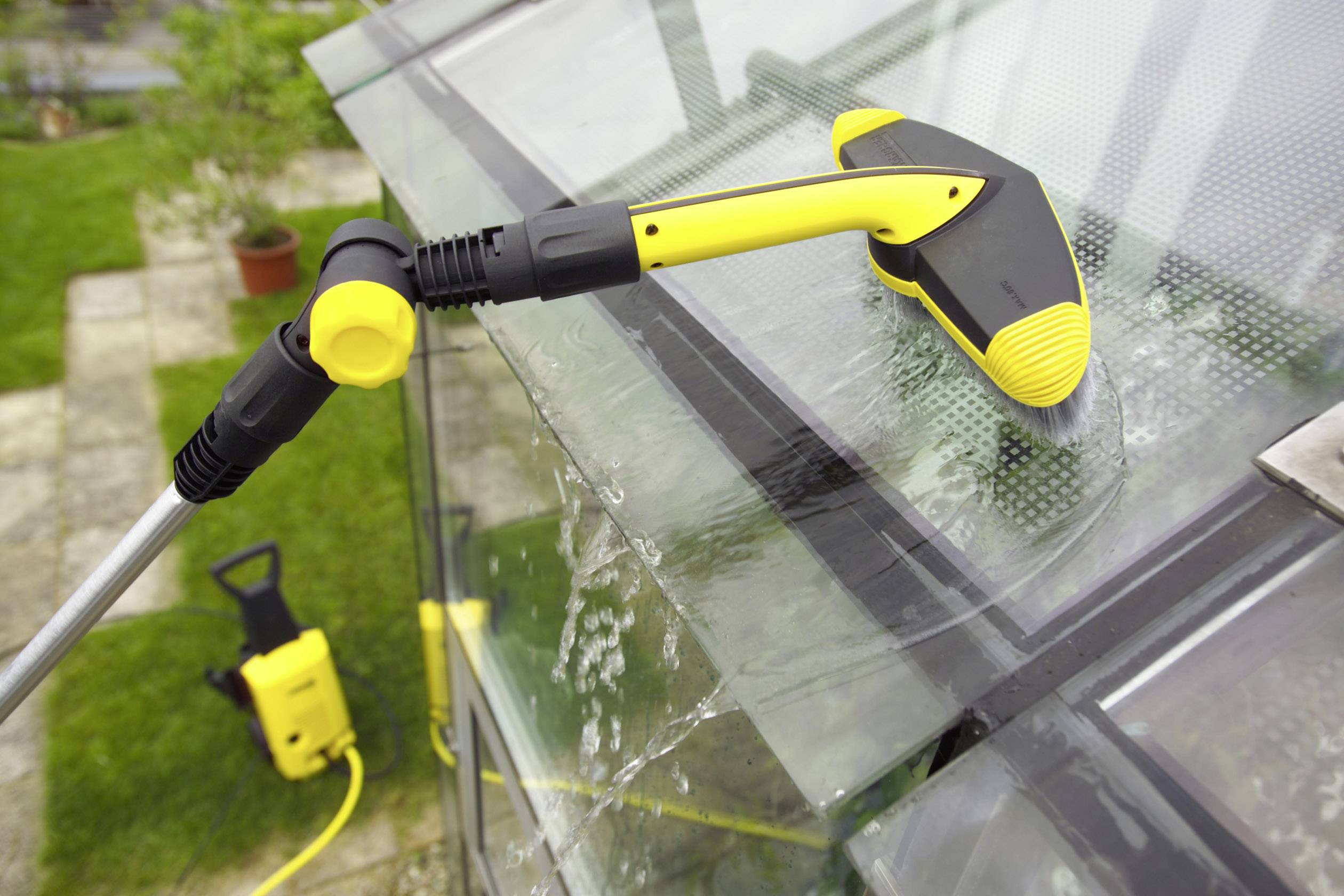 Ein Fensterreiniger reinigt mit einem elektrischen Hochdruckreiniger ein Glasdach. Wasserspritzer sind sichtbar.