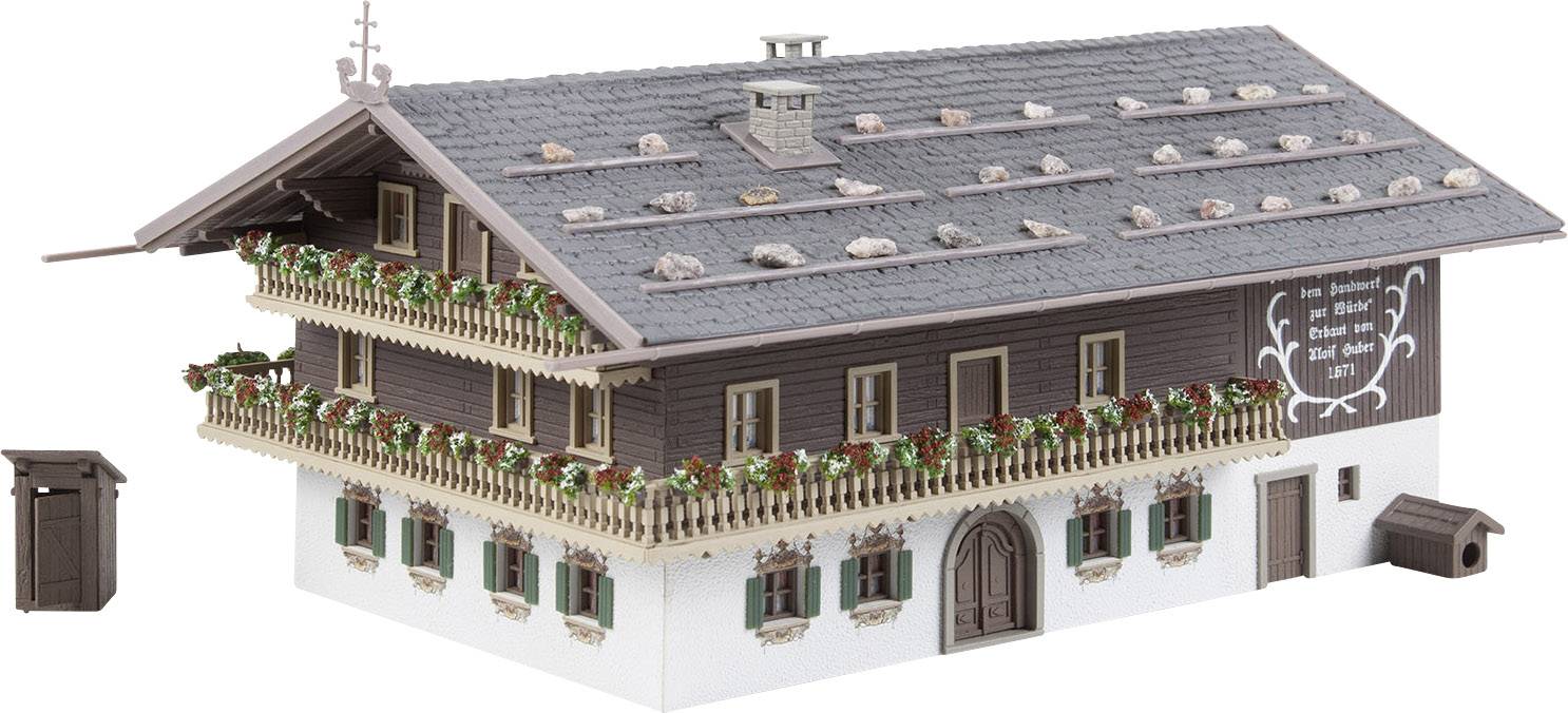 Modell eines traditionellen alpenländischen Hauses mit Holzverzierungen, Blumenkästen und Schieferdach. Ein kleines Nebengebäude steht seitlich.