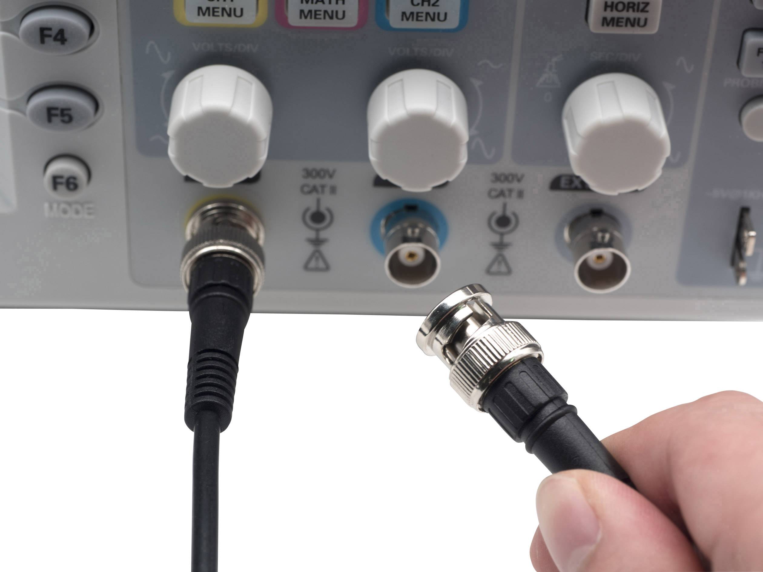 Eine Hand hält einen Kabelstecker, der an ein Messgerät mit mehreren Drehknöpfen angeschlossen wird. Symbole und Anschlüsse sind sichtbar.