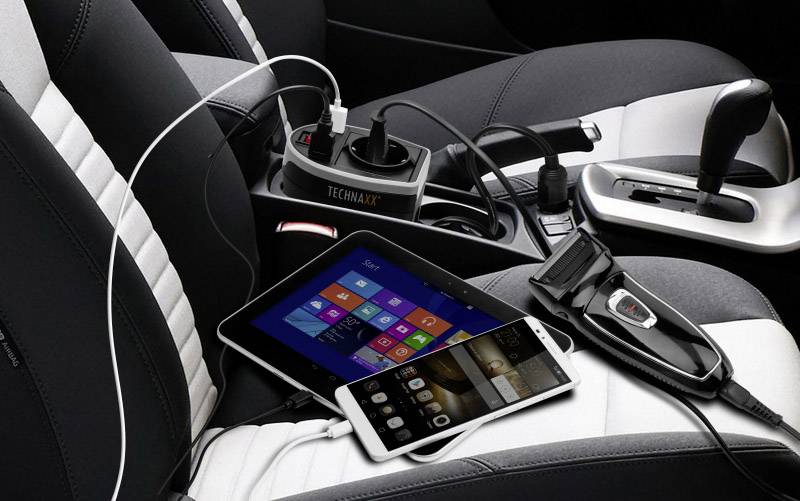 Ein Auto-Innenraum mit angeschlossener Steckdosenleiste. Tablet und Smartphone werden gleichzeitig geladen, ein Rasierapparat ist eingesteckt.