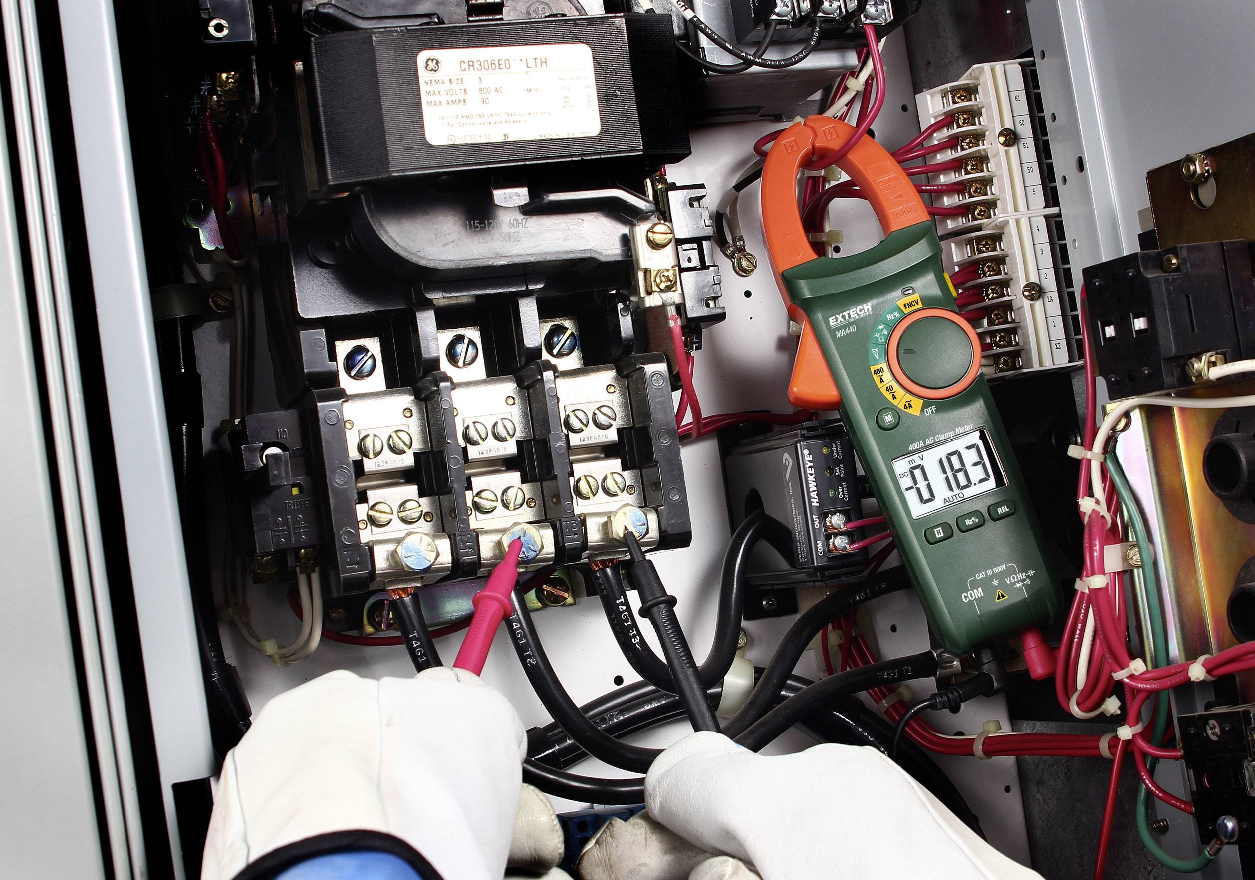 Ein Elektriker misst den elektrischen Strom mit einem Multimeter in einem Schaltkasten. Der Wert auf dem Display zeigt 18,3.