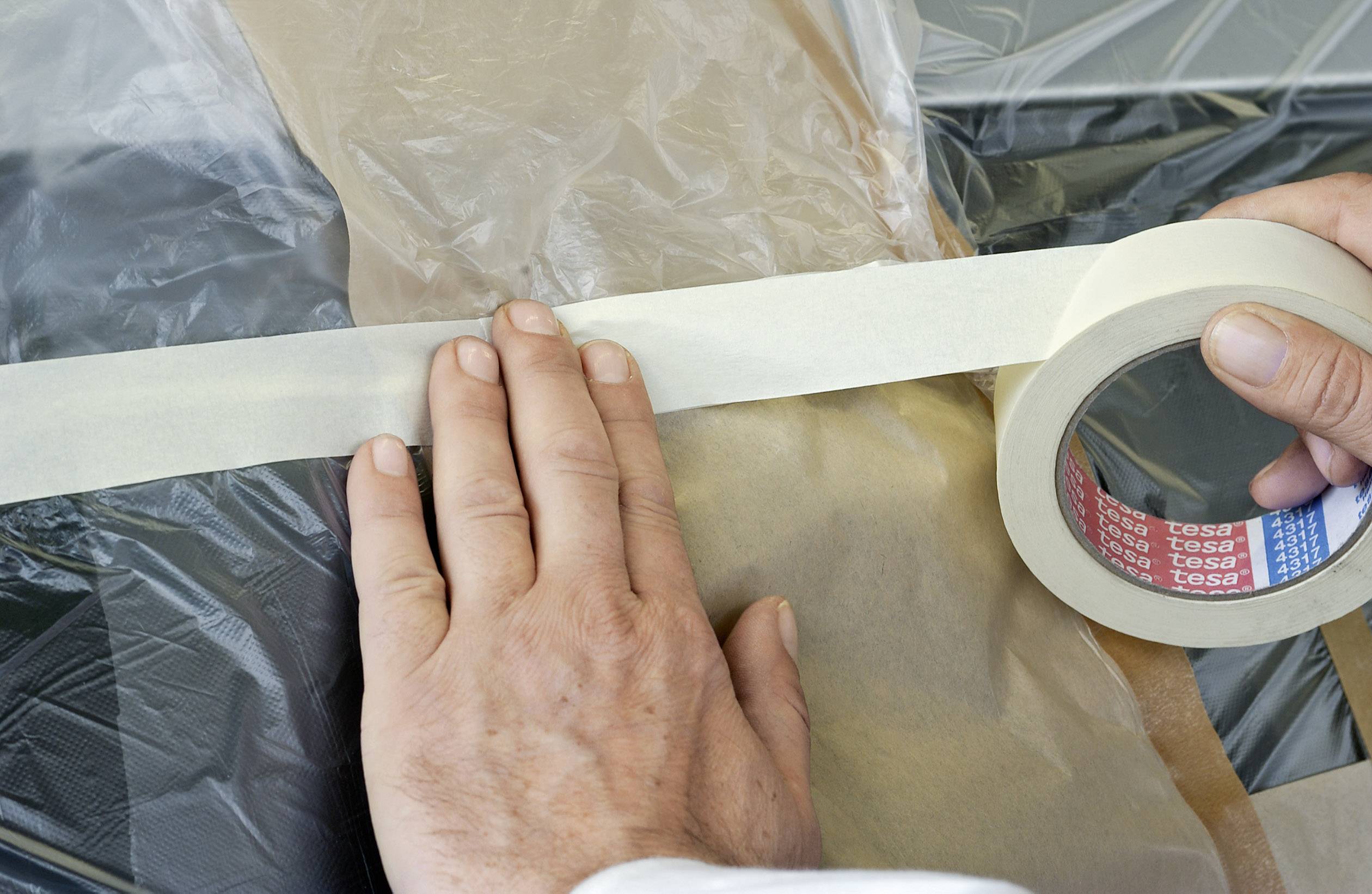 Eine Person klebt Kreppband auf eine Plastikfolie, um Oberflächen zu schützen, wahrscheinlich beim Malen oder Renovieren.