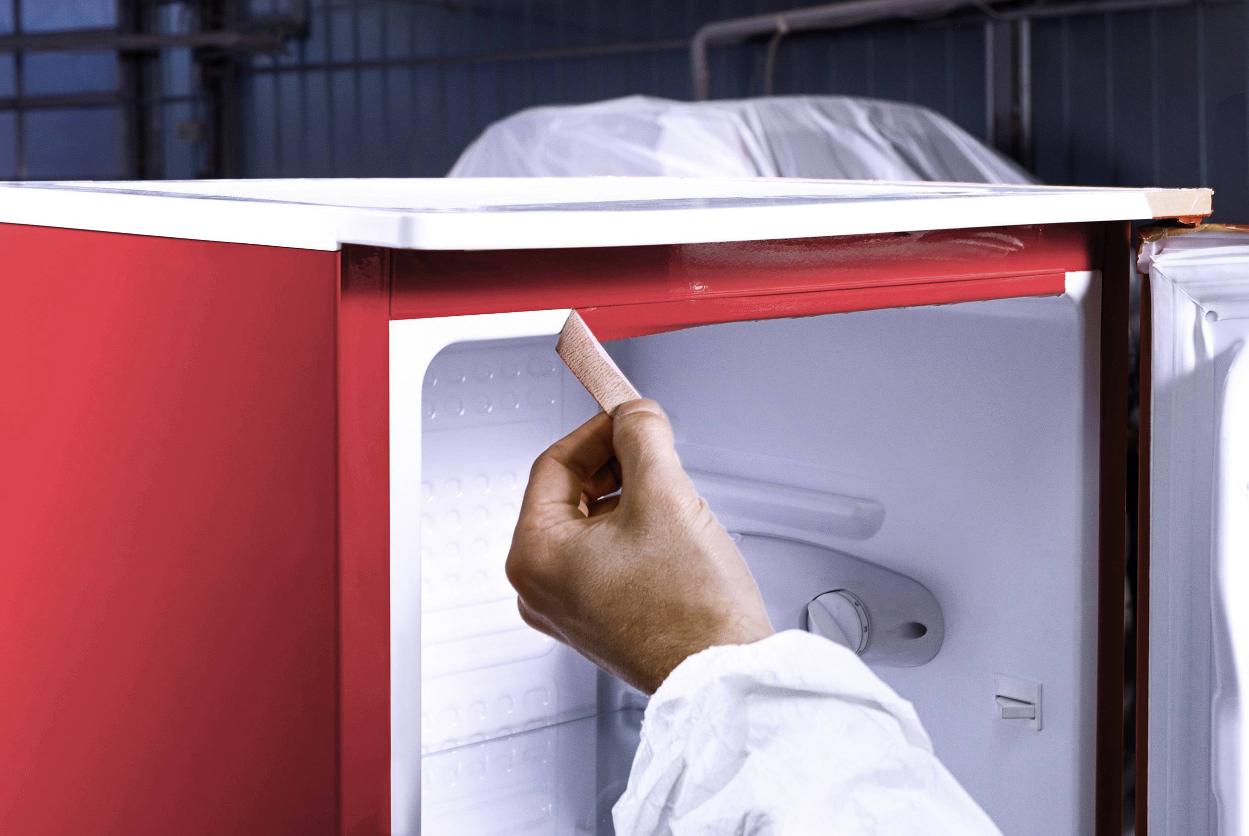 Eine Hand in Schutzkleidung überprüft die Dichtung eines geöffneten roten Kühlschranks in einem Labor- oder industriellen Umfeld.