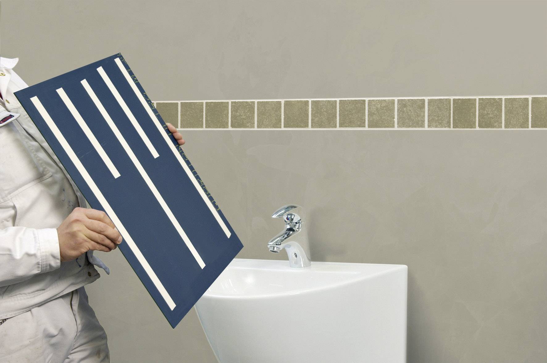 Person hält Fliesenschablone mit gleichmäßigen Streifen vor einer Wand mit rechteckigen, diagonalen Fliesen über einem Waschbecken.