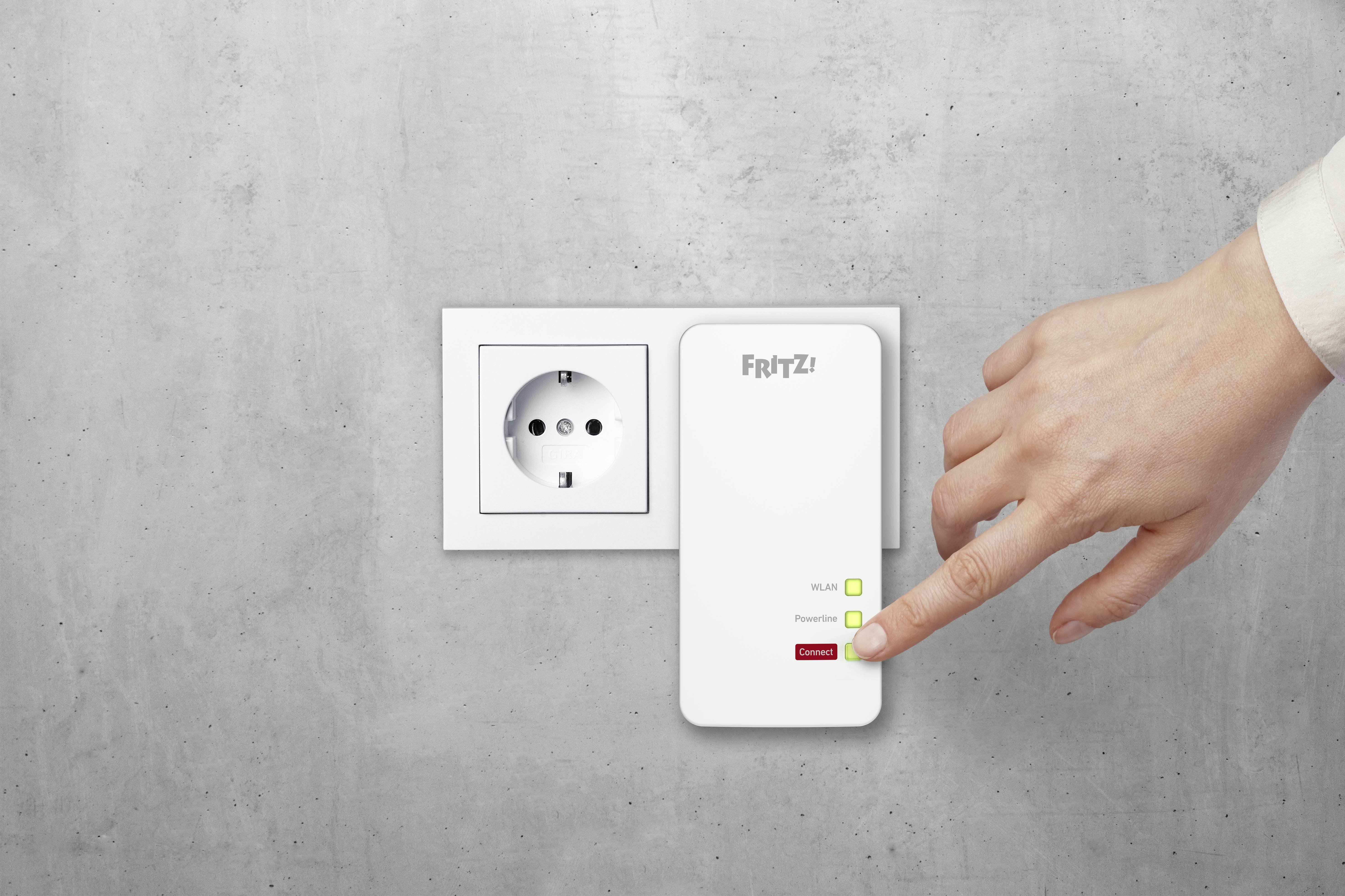 Eine Hand drückt den WPS-Knopf auf einem Fritz! WLAN-Repeater, der in eine Steckdose neben einer anderen Steckdose eingesteckt ist.