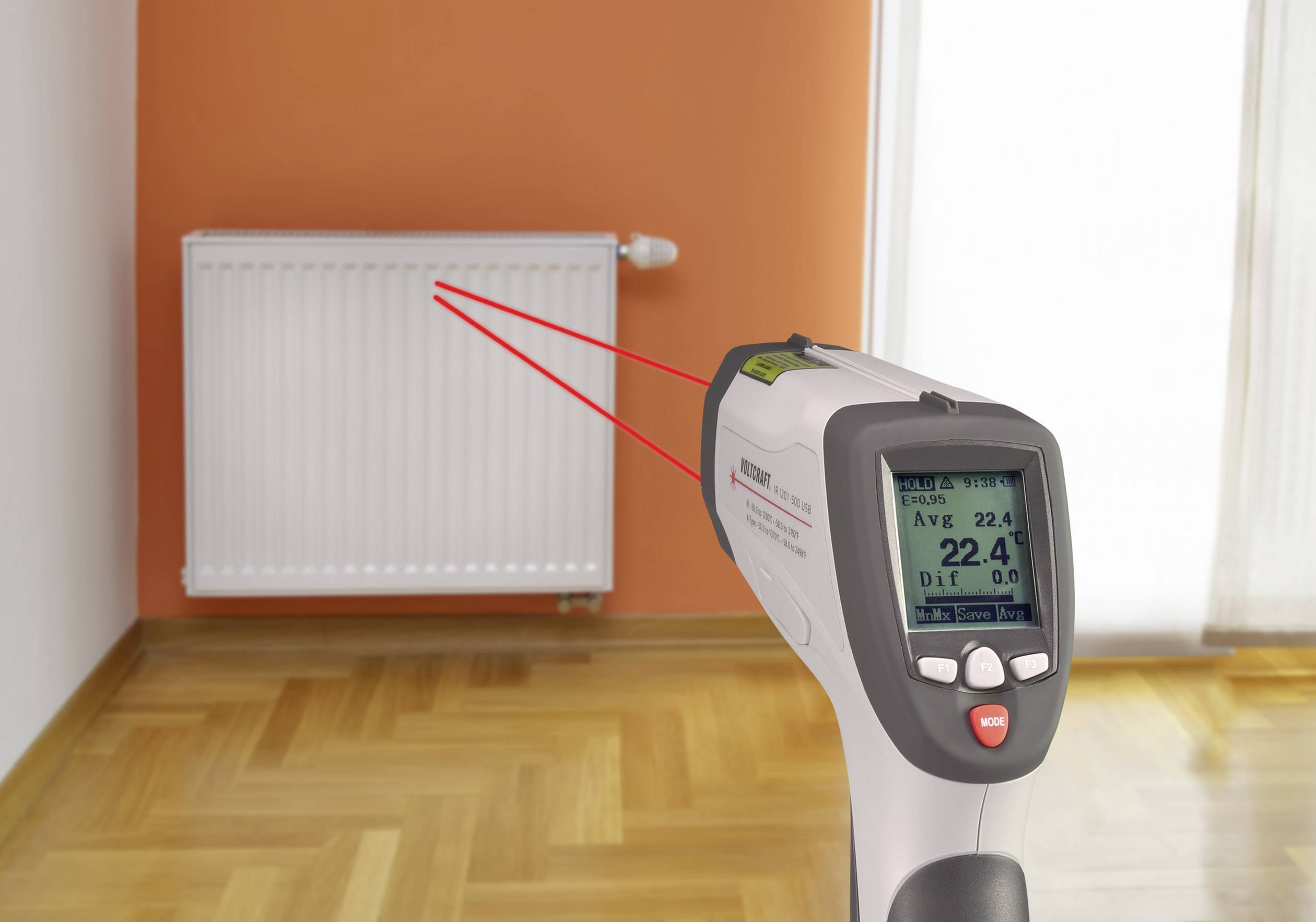 Ein Infrarot-Thermometer misst die Oberflächentemperatur eines Heizkörpers in einem Raum mit Holzboden und orangefarbener Wand.