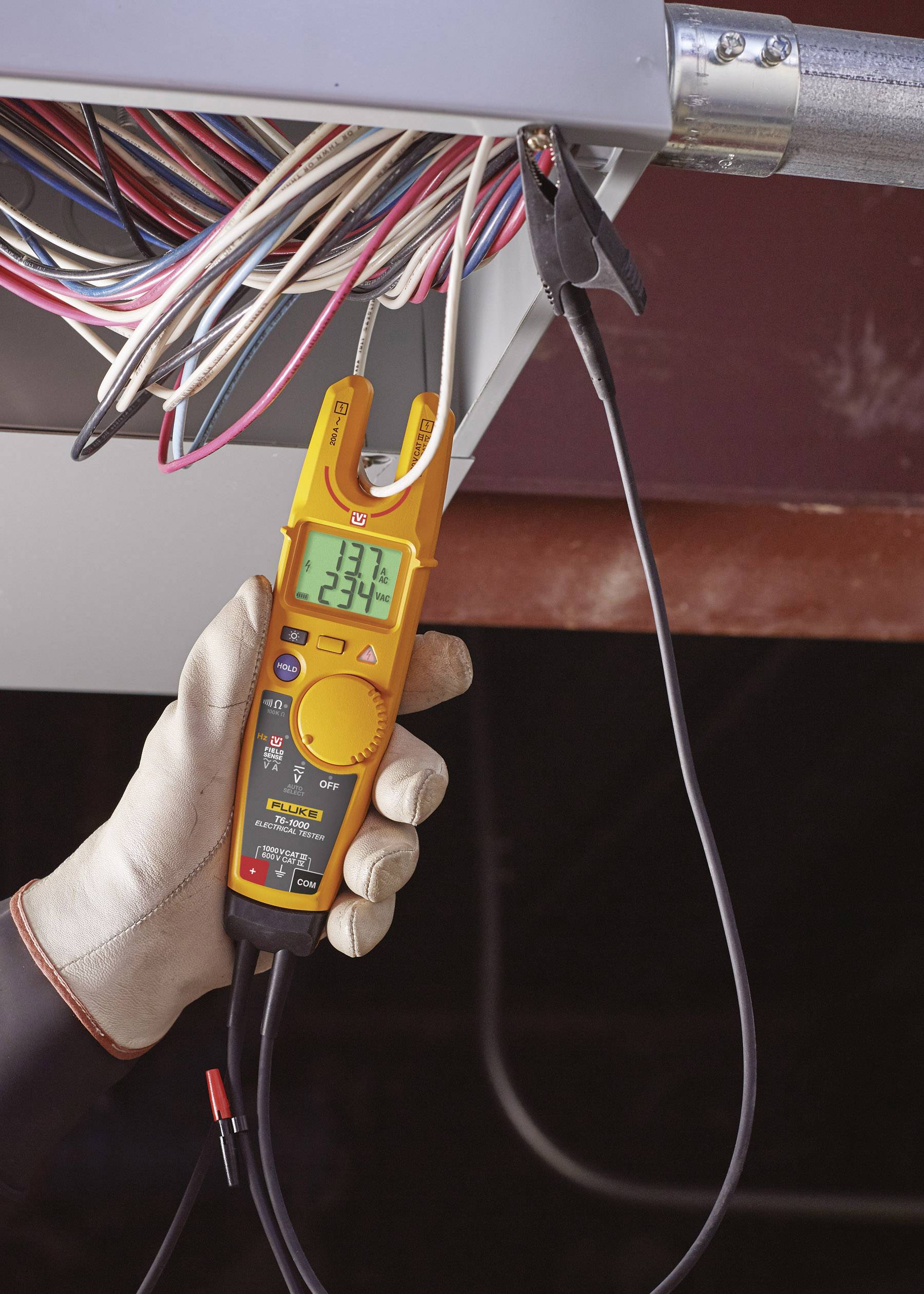 Elektriker misst Spannung an einer Schalttafel mit einem digitalen Multimeter. Der Messwert auf dem Display zeigt 234 Volt an.