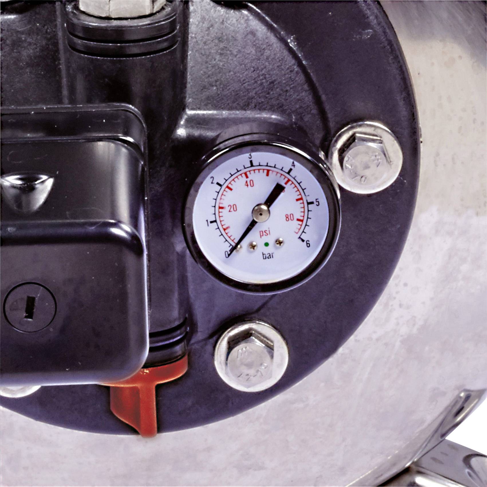 Ein Manometer an einem Metallkessel zeigt einen Druck von etwa 20 psi an. Das Manometer ist von mehreren Schrauben umgeben.