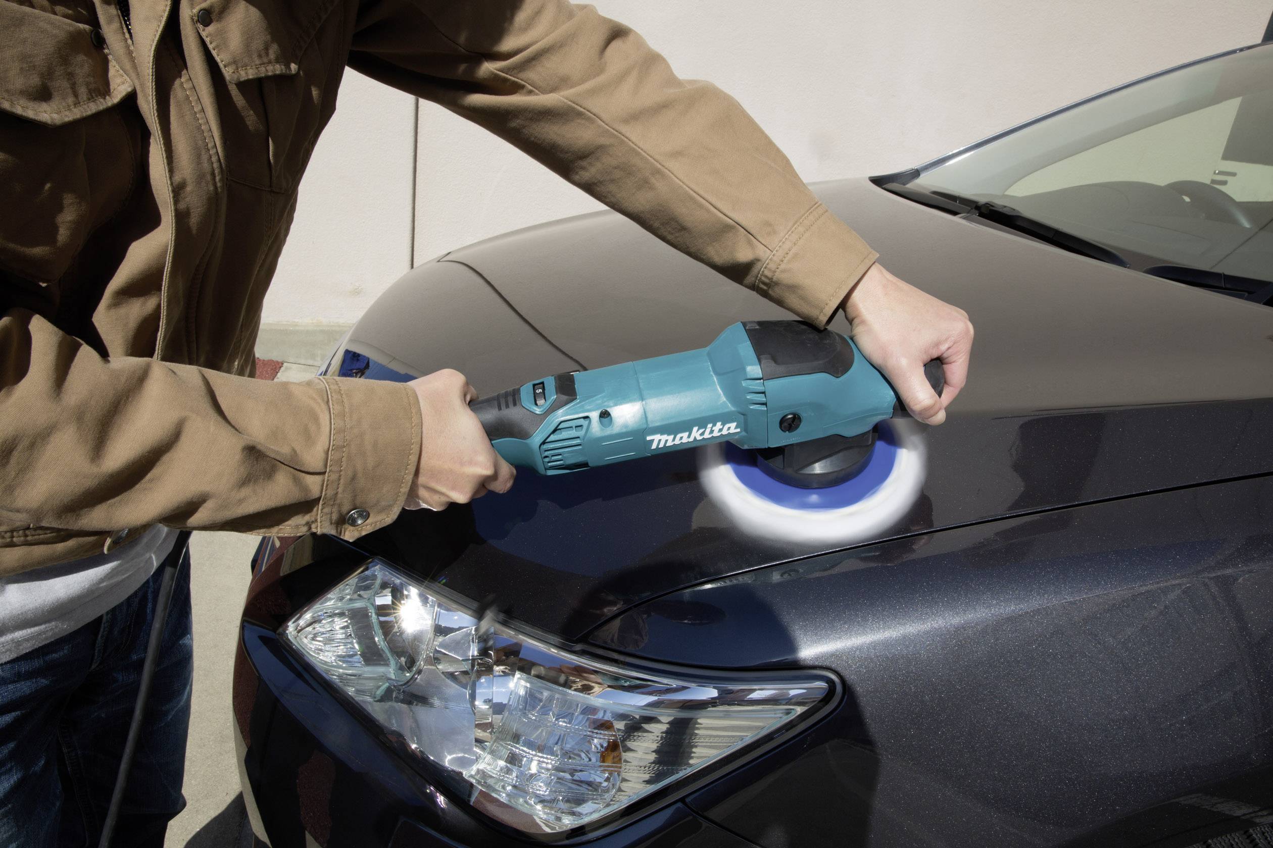 Person poliert Auto mit blauem Werkzeug auf der Motorhaube. Der Lack wird glänzend und sauber.