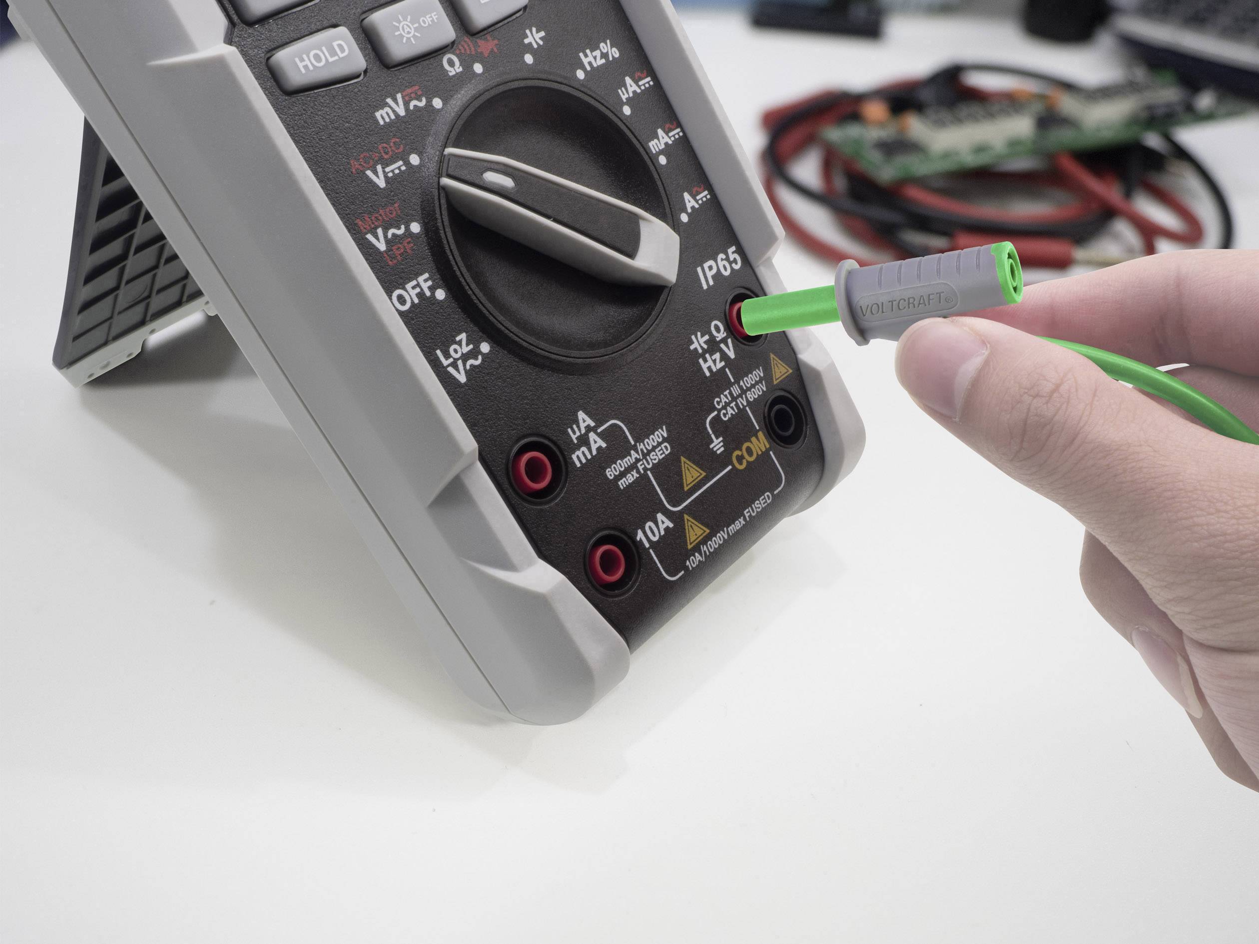 Eine Person hält ein grünes Messkabel, das in ein Multimeter gesteckt ist, um Spannungsmessungen durchzuführen.