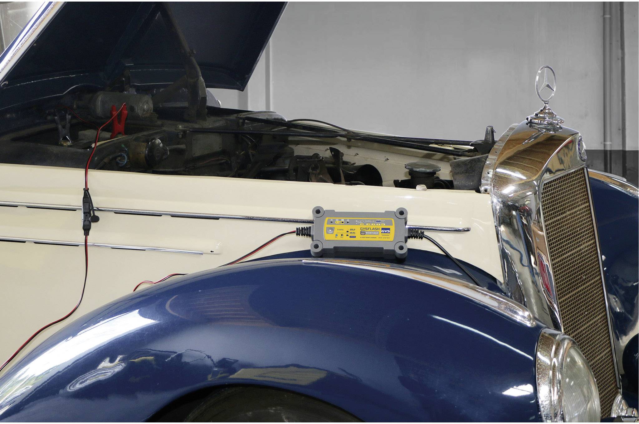 Ein altes Auto mit geöffneter Motorhaube wird mit einem Ladegerät aufgeladen.