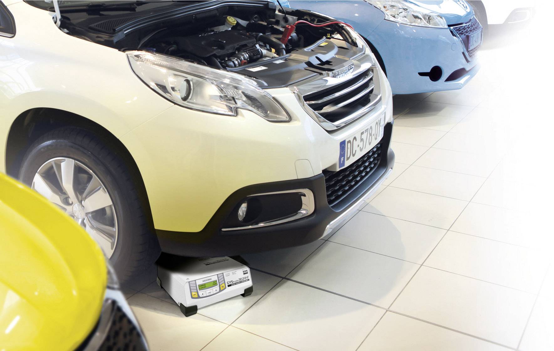 Ein Auto steht in einer Werkstatt mit geöffneter Motorhaube, das Motorprüfgerät ist unten am Auto platziert, prüft die Batterie.