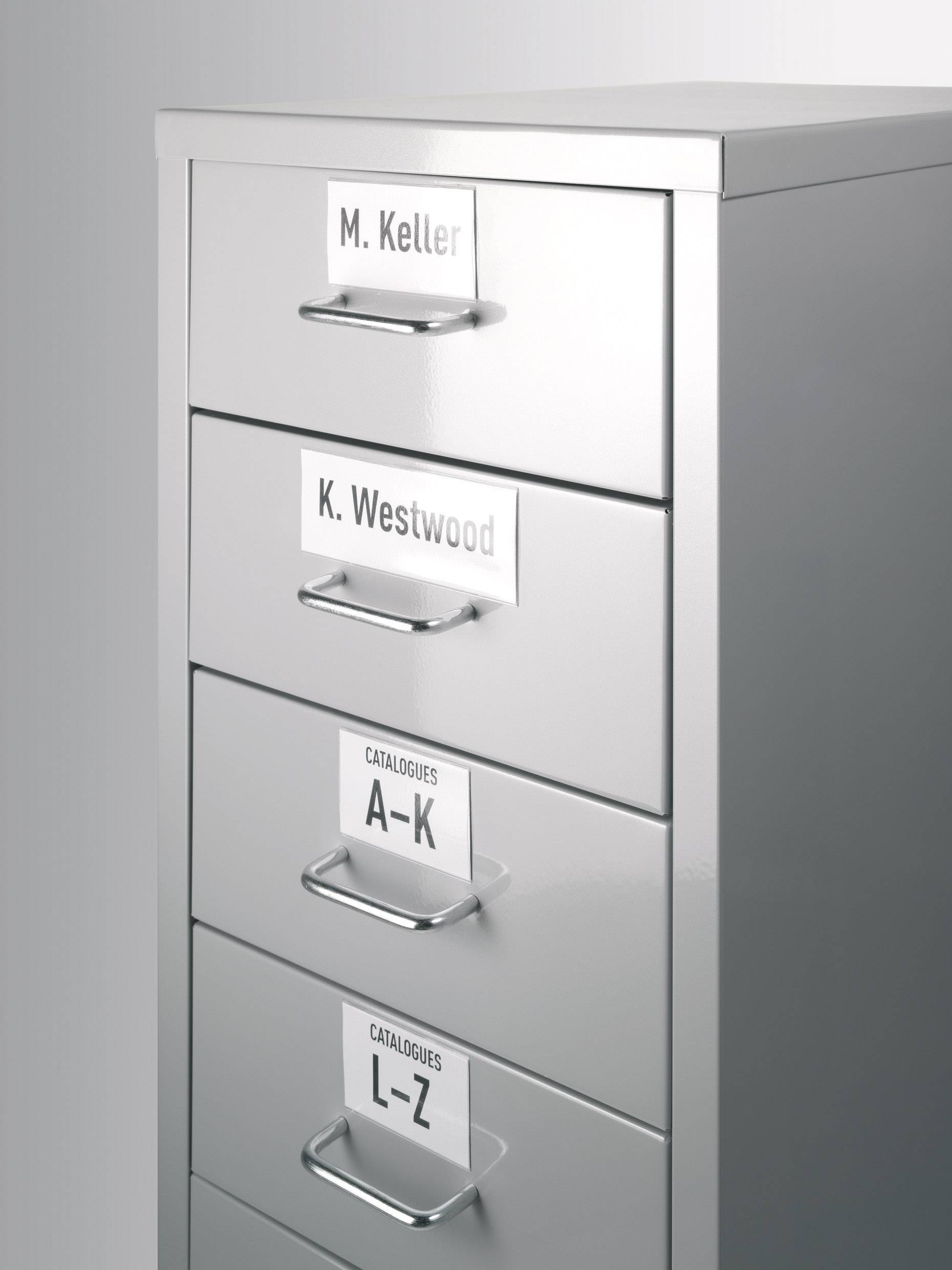 Ein silberner Aktenschrank mit vier Schubladen, beschriftet von oben nach unten: 'M. Keller', 'K. Westwood', 'Catalogues A-K', 'Catalogues L-Z'.