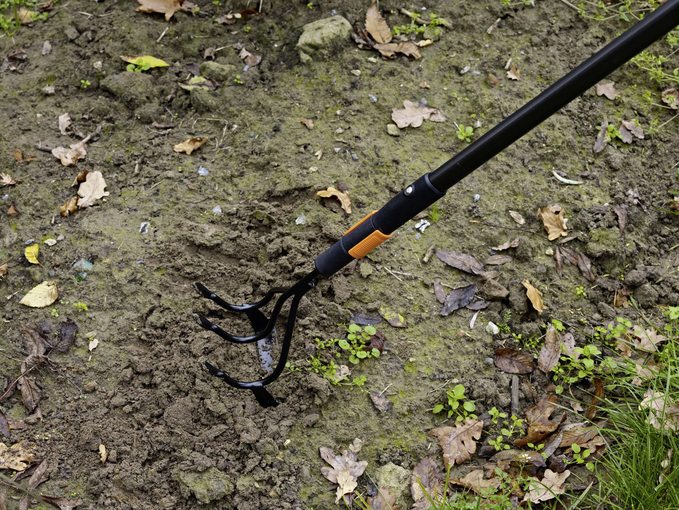 Ein Rechen bearbeitet den Boden in einem Garten, umgeben von Blättern und Gras.