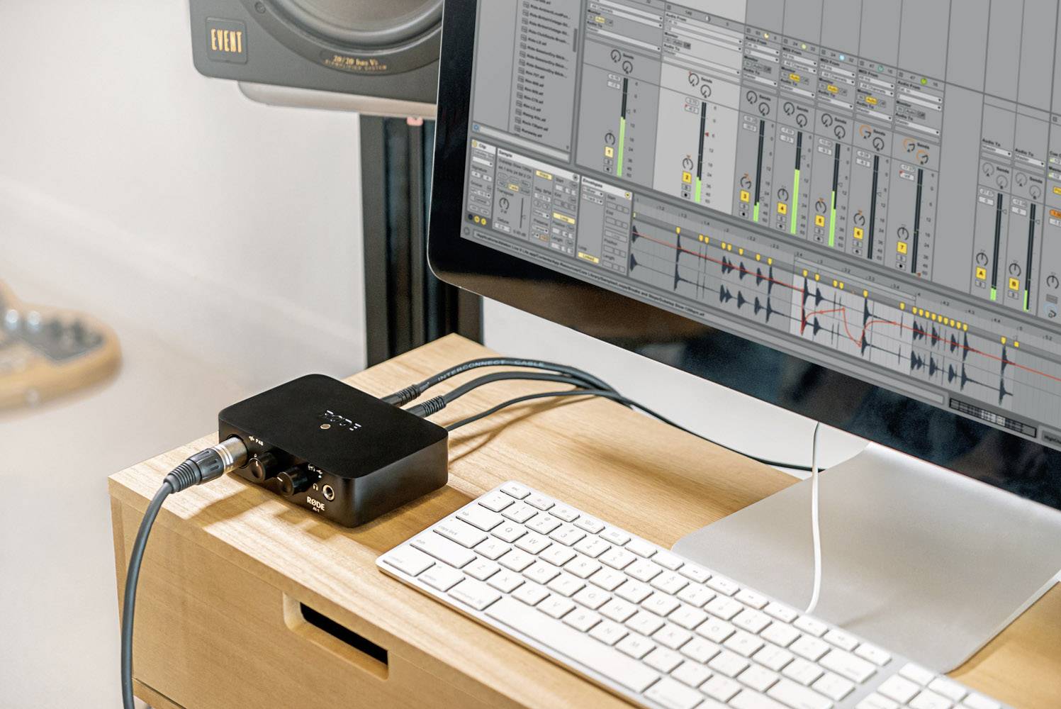 Ein Computerbildschirm zeigt ein digitales Audio-Workstation-Interface mit mehreren Spuren. Ein Audio-Interface steht daneben, verbunden mit Kabeln.