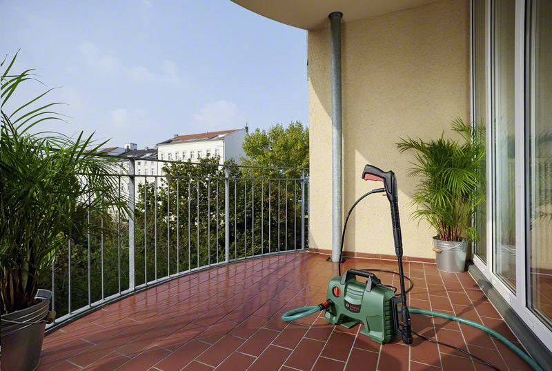 Ein Hochdruckreiniger steht auf einem Balkon mit Blick auf grüne Bäume und ein Gebäude.