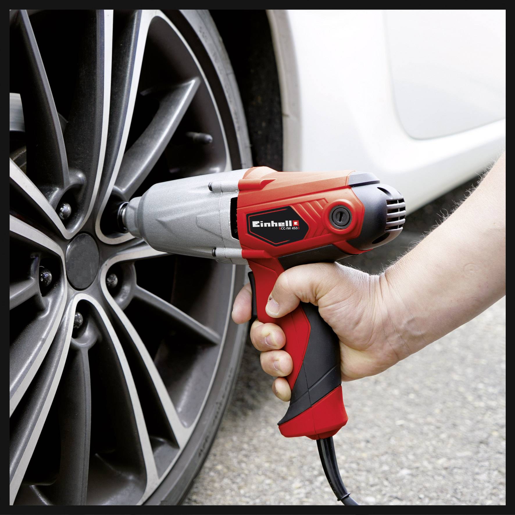Eine Hand benutzt einen roten elektrischen Schlagschrauber, um eine Radmutter an einem Autoreifen festzuziehen.