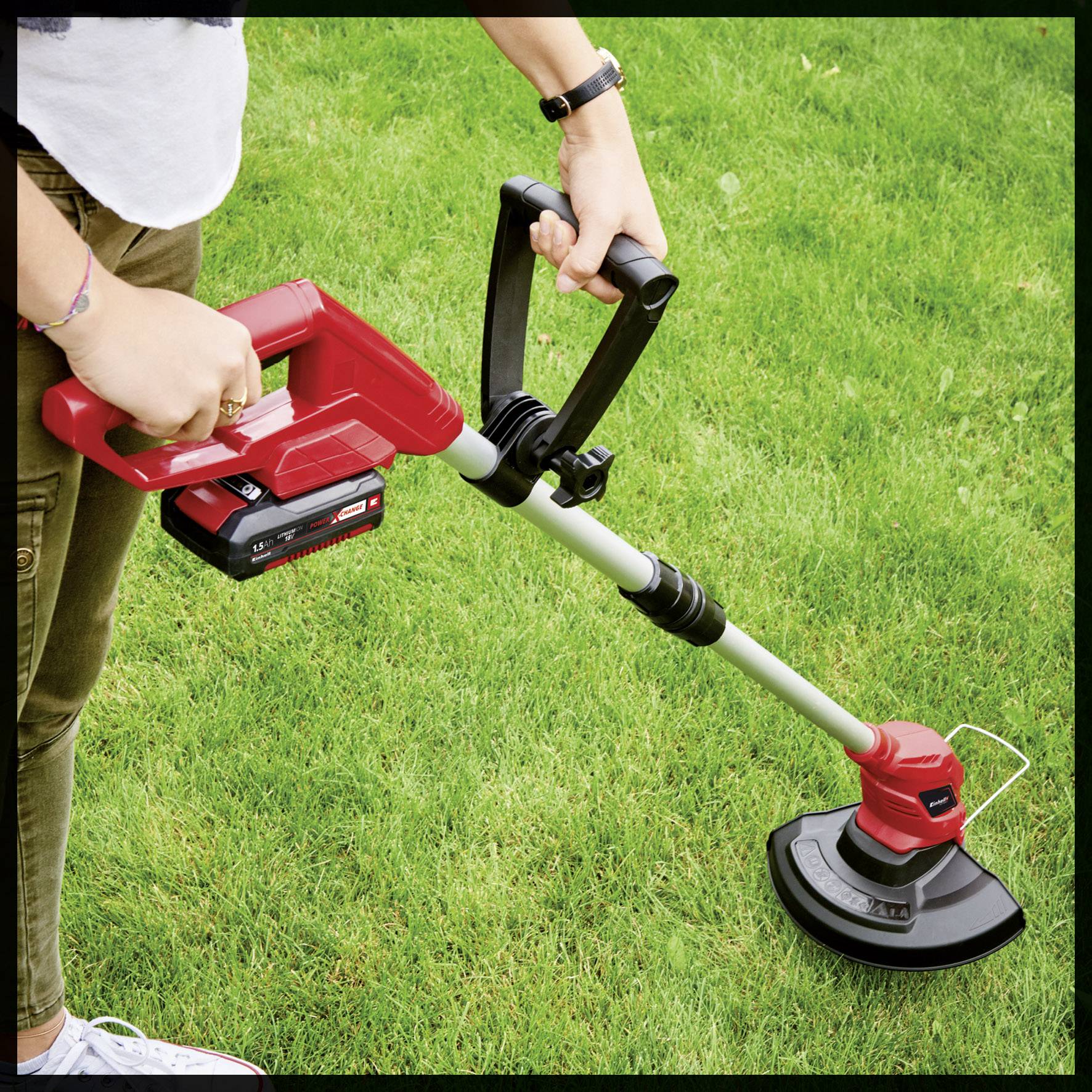 Eine Person schneidet mit einem roten, elektrischen Rasentrimmer das Gras im Garten. Geräteakku ist am Trimmer befestigt.