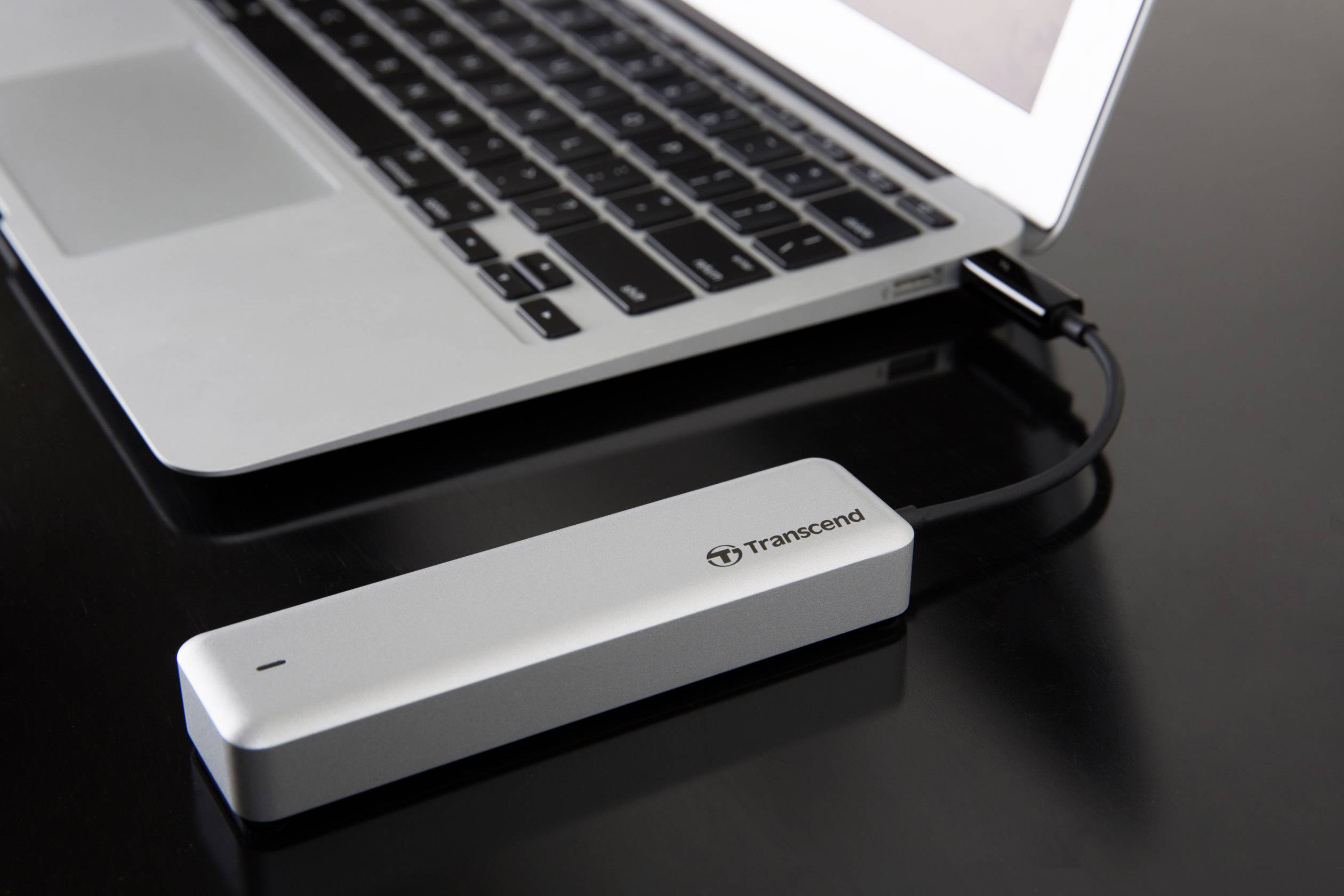 Externe Festplatte in silbernem Gehäuse, angeschlossen an einen Laptop auf einem schwarzen Tisch; Symbol für Datenspeicherung.