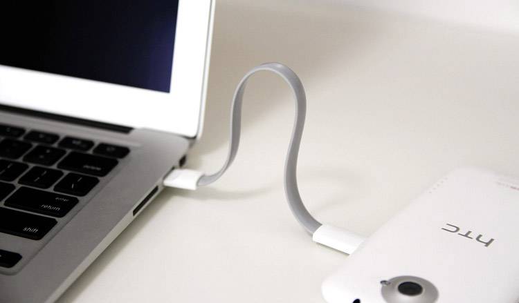 Ein Laptop ist mit einem Smartphone durch ein graues USB-Kabel verbunden, das leicht gebogen ist.