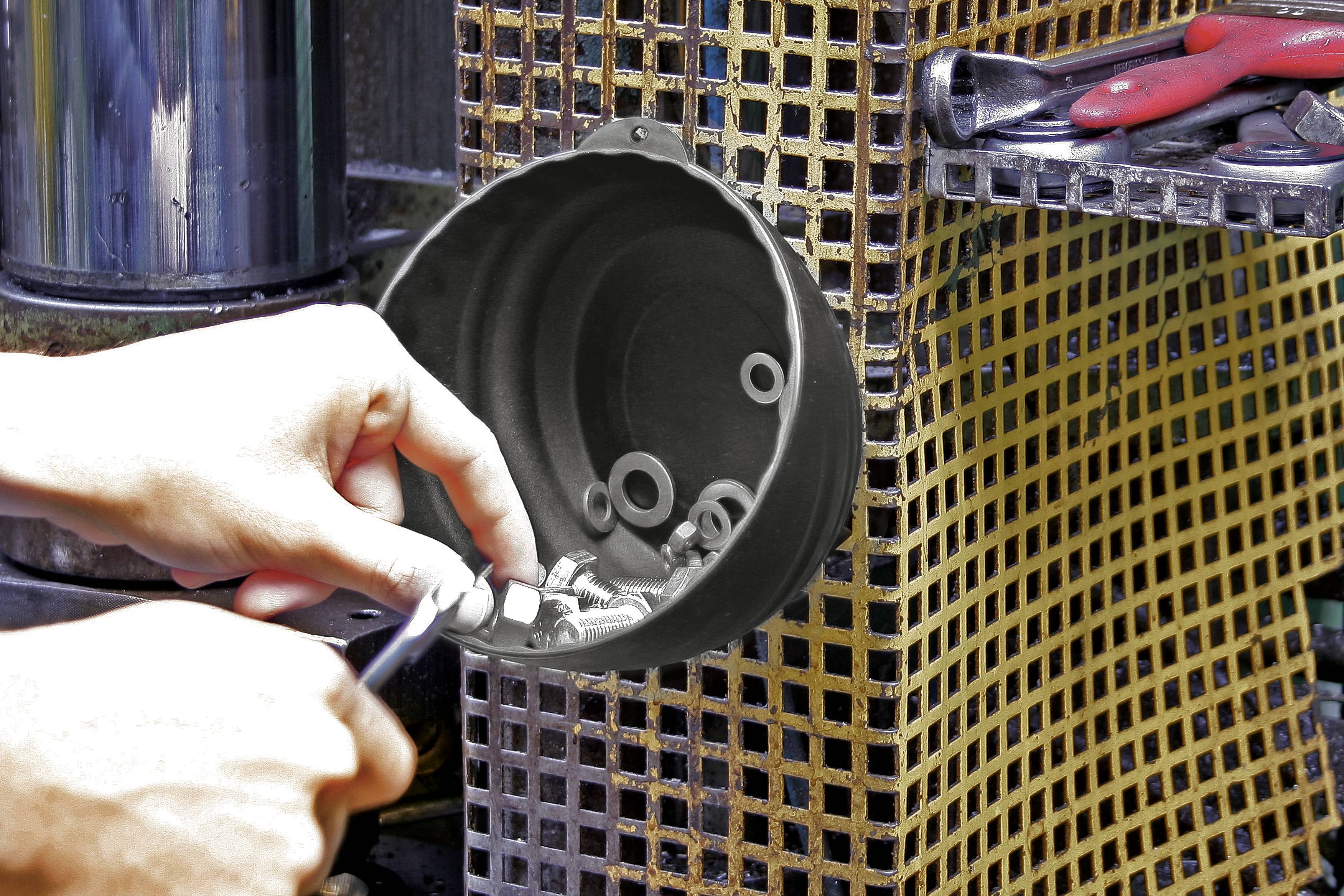 Person hält Schraubenzieher und sortiert Schrauben in eine Metallschale. Im Hintergrund ein Regal mit Handwerkzeugen.