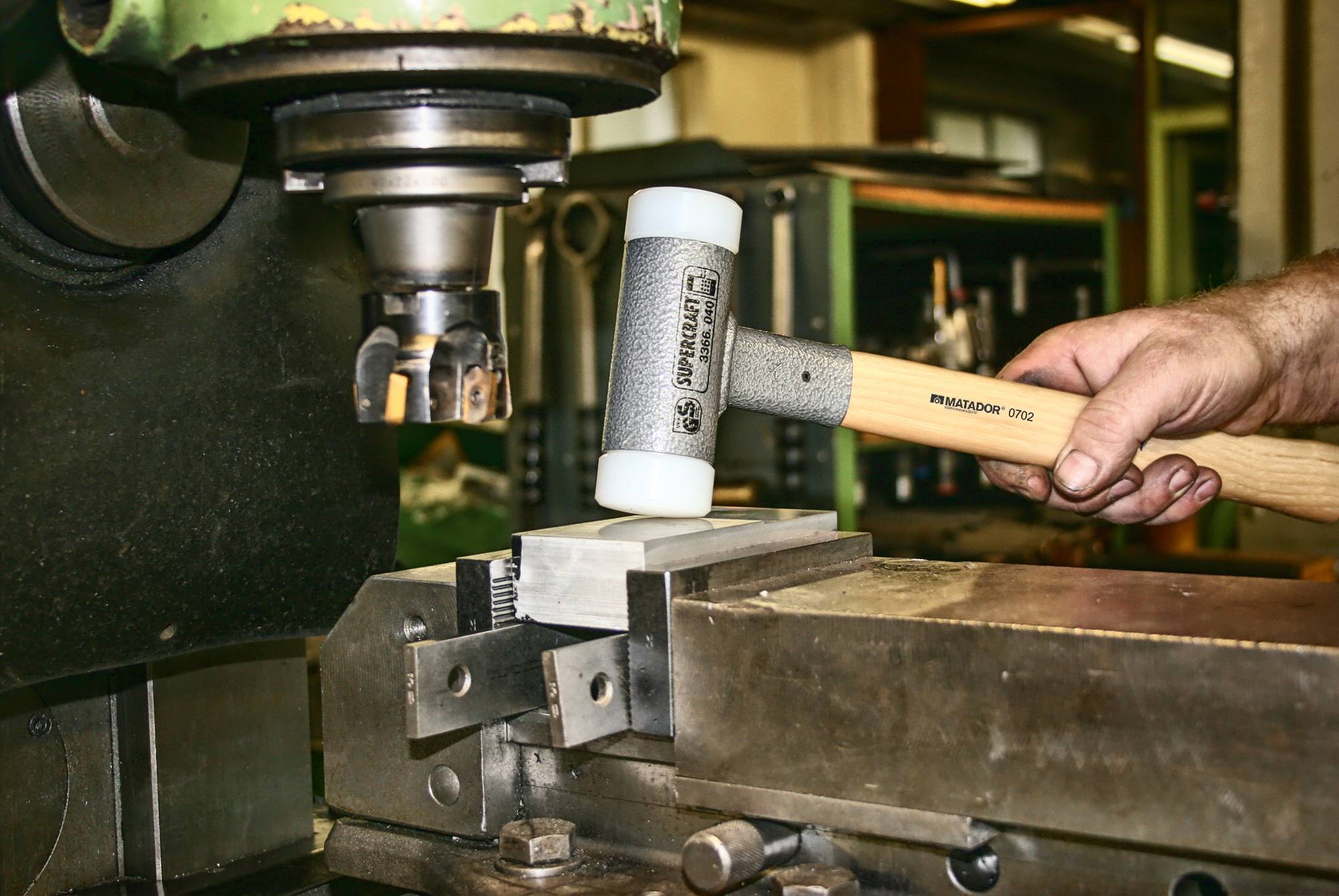 Eine Hand hält einen Schonhammer und richtet ein Metallstück in einer industriellen Maschinenwerkstatt aus.