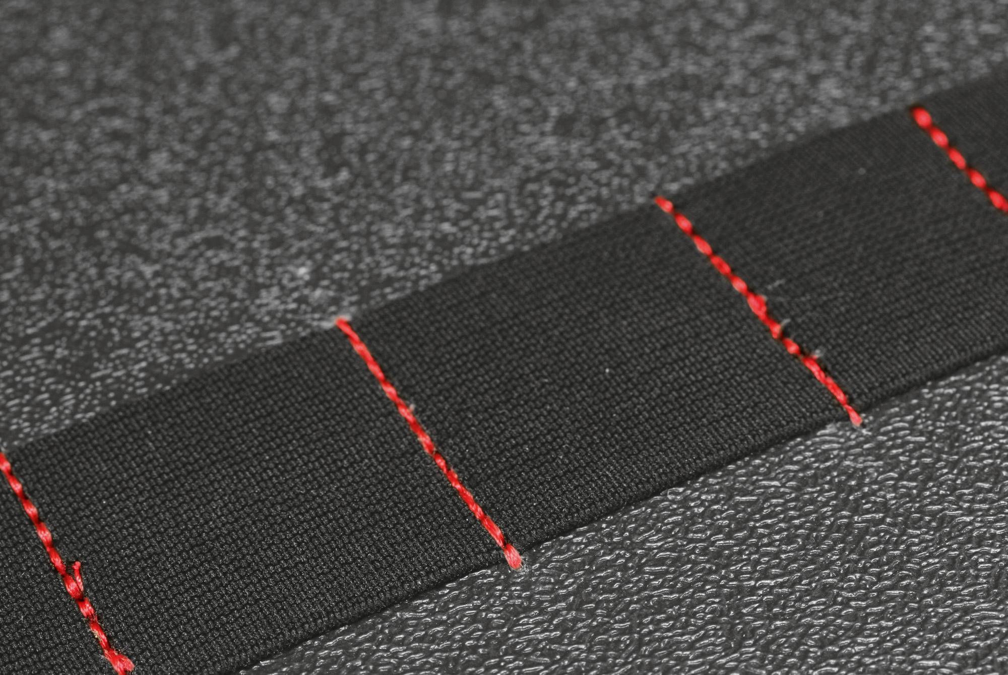 Ein schwarzes Band mit roten Nähten, auf einem strukturierten grauen Hintergrund liegend, zeigt Aufmerksamkeit auf Details in Textilien.
