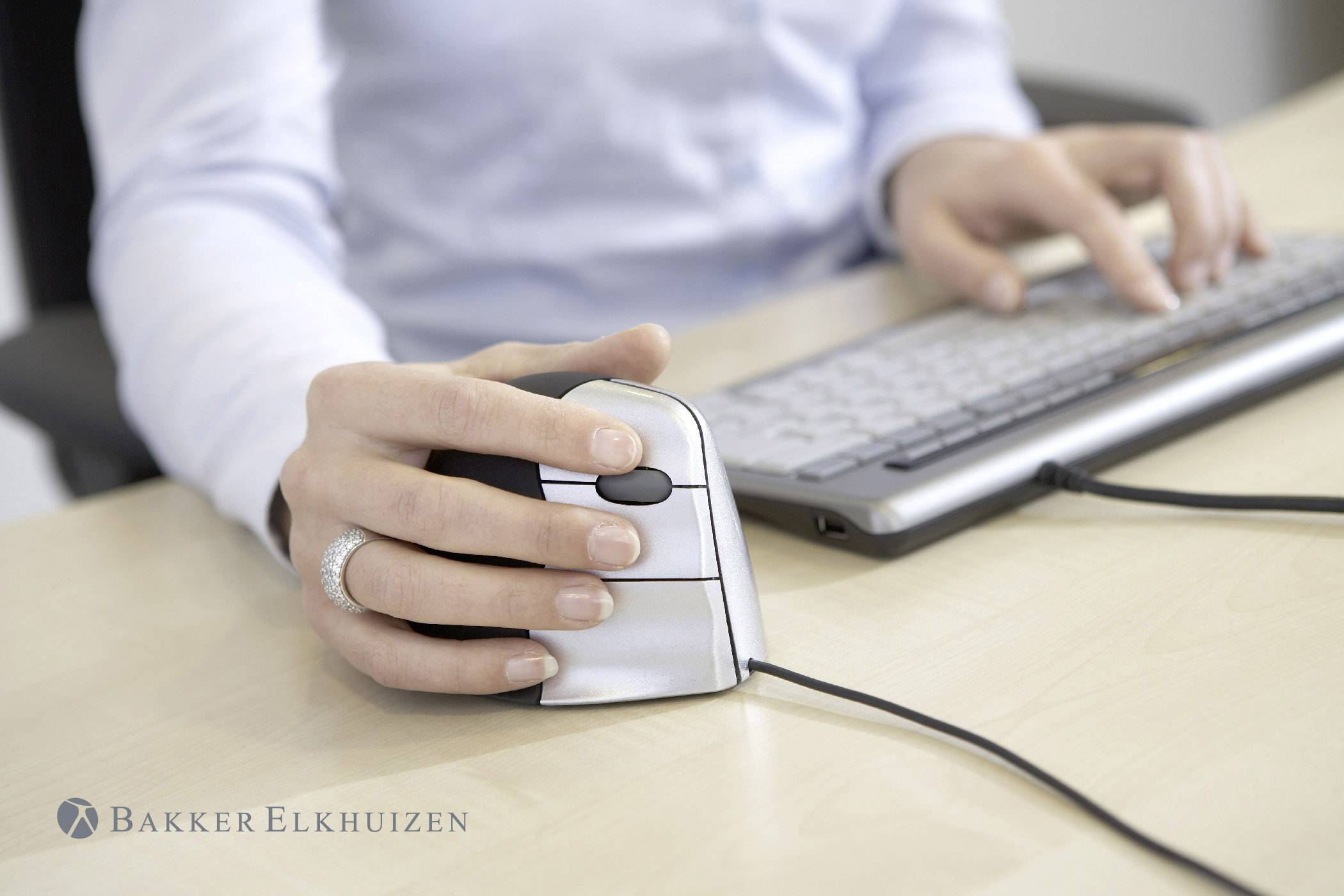 Person hält ergonomische Maus in der rechten Hand und tippt auf einer Tastatur. Ergonomisches Design für komfortable Nutzung.