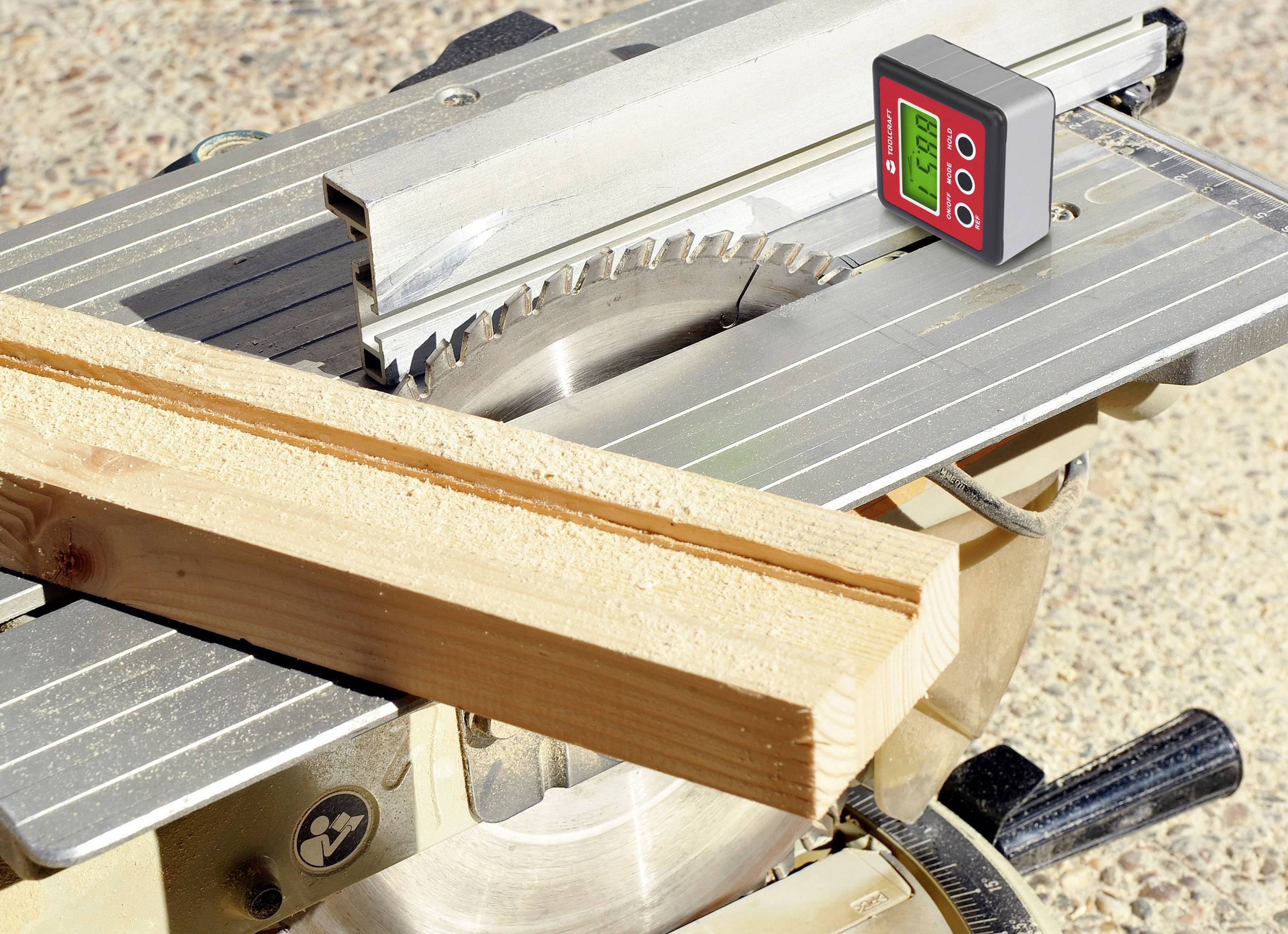 Elektrische Kreissäge mit Holzbrett auf dem Tisch. Ein digitales Messgerät zeigt Winkel an.