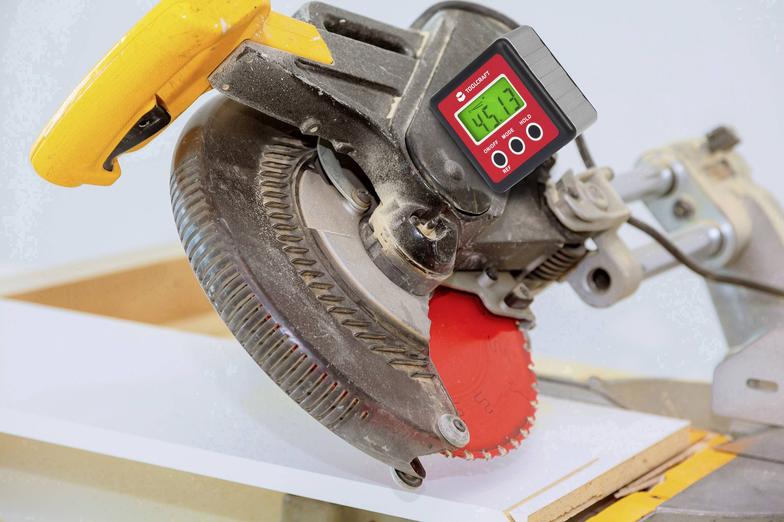 'Kreissäge schneidet Holzplatte' – Ein Bild einer elektrischen Kreissäge mit rotem Sägeblatt, das eine weiße Holzplatte schneidet. Oben ist am Gerät eine digitale Anzeige zu sehen.