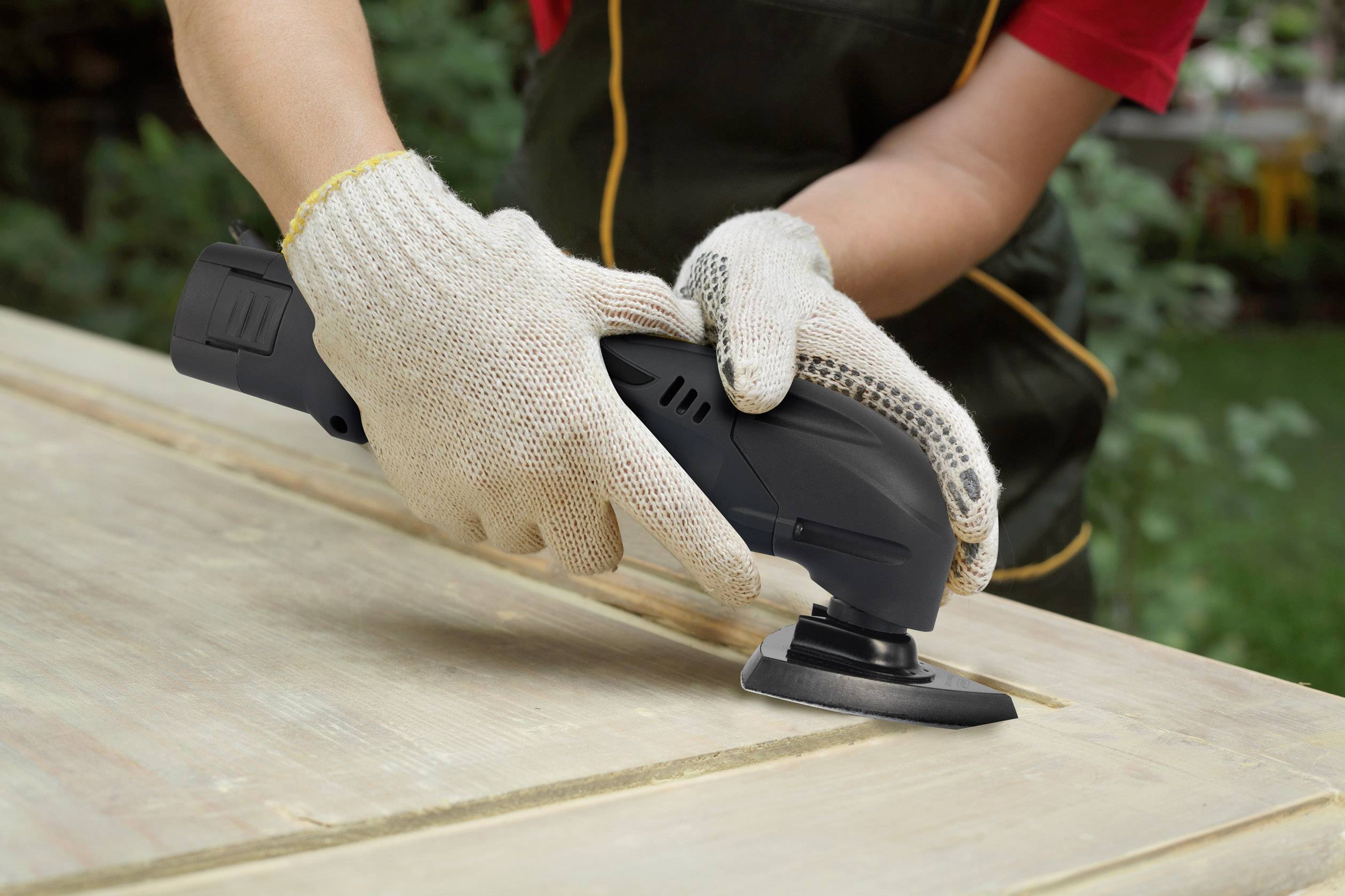 Person mit Handschuhen schleift Holzoberfläche mit Elektrowerkzeug.