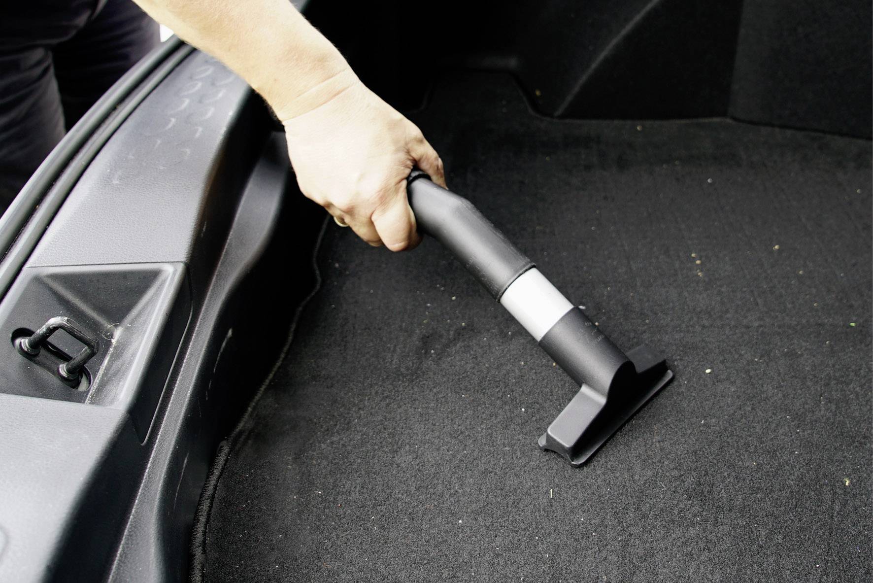 Person reinigt den Kofferraum eines Autos mit einem Staubsauger.