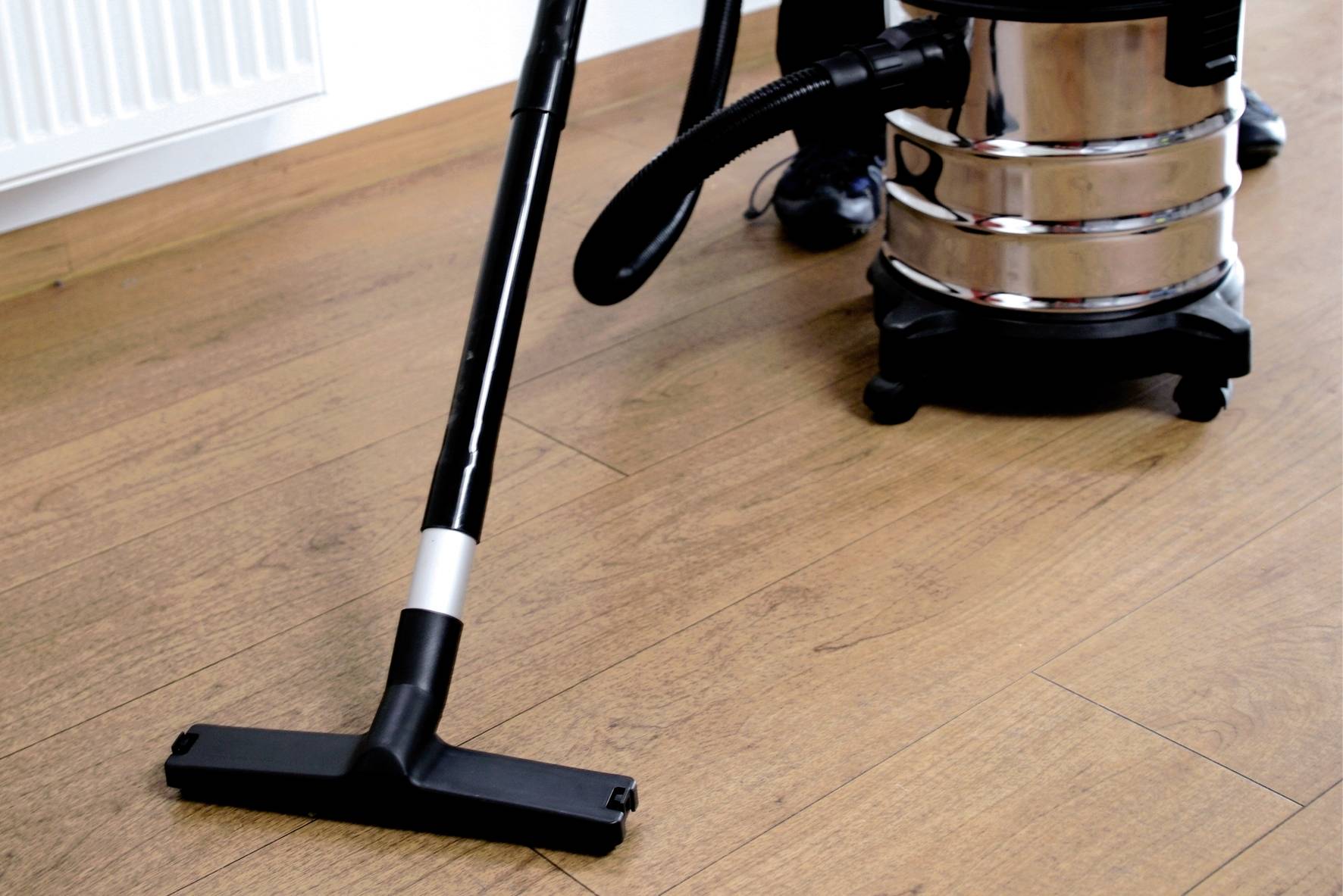 Eine Person reinigt einen Holzboden mit einem schwarzen Staubsauger. Der Raum wirkt sauber und ordentlich.