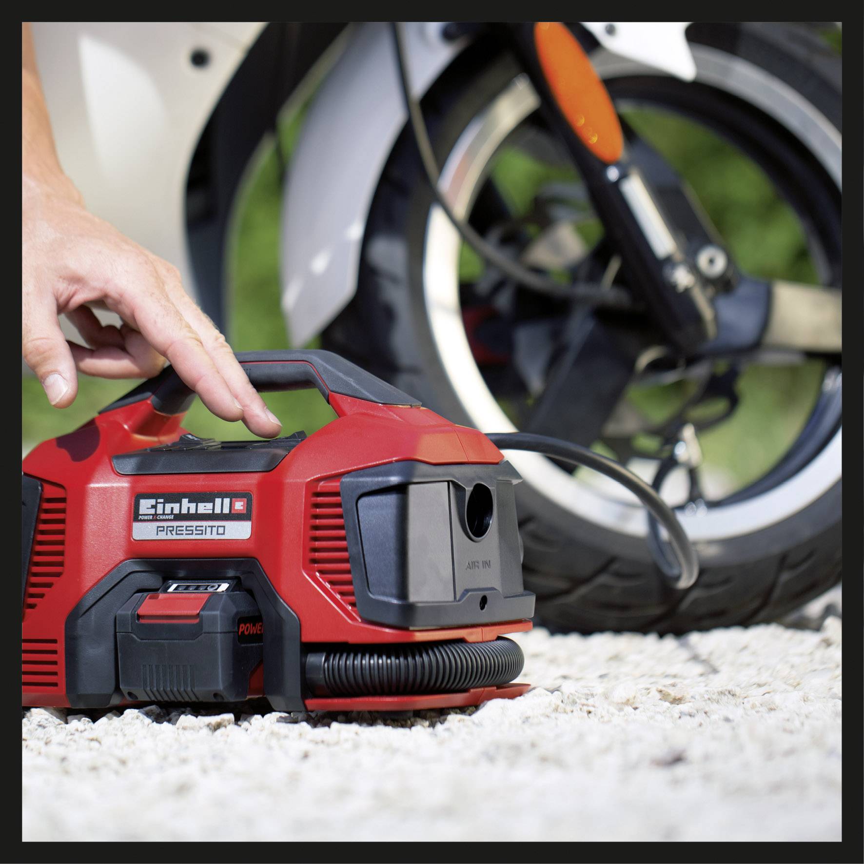 Eine Person nutzt einen tragbaren Kompressor, um einen Motorradreifen zu befüllen. Der Kompressor ist rot und handlich.