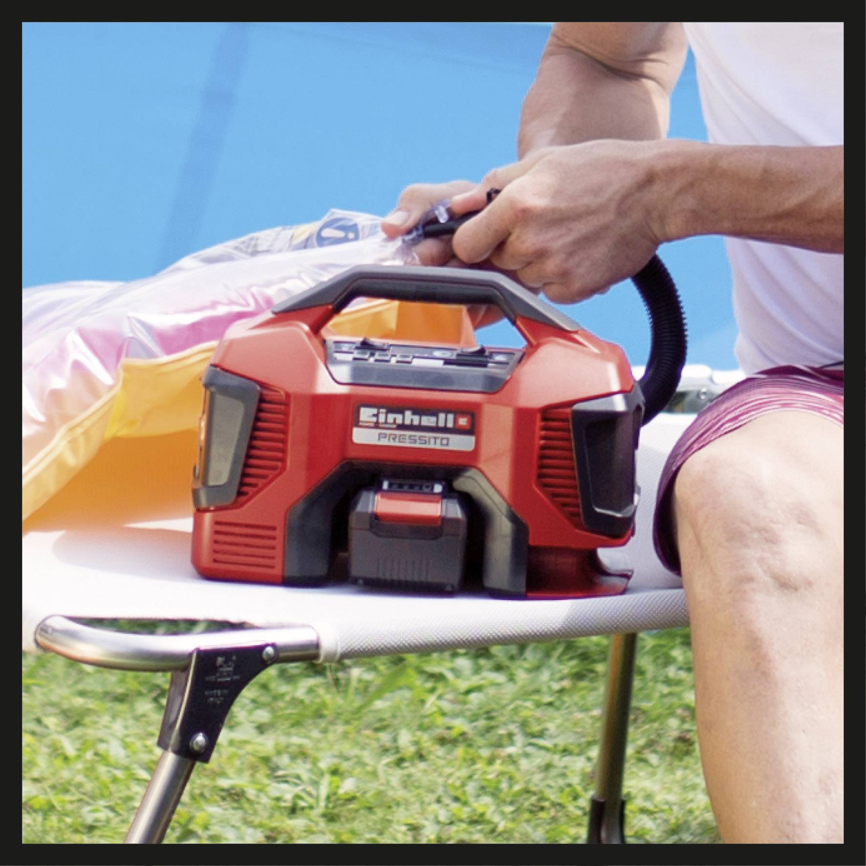 Eine Person nutzt eine rote elektrische Luftpumpe auf einer Liege im Freien, um ein aufblasbares Objekt zu füllen.