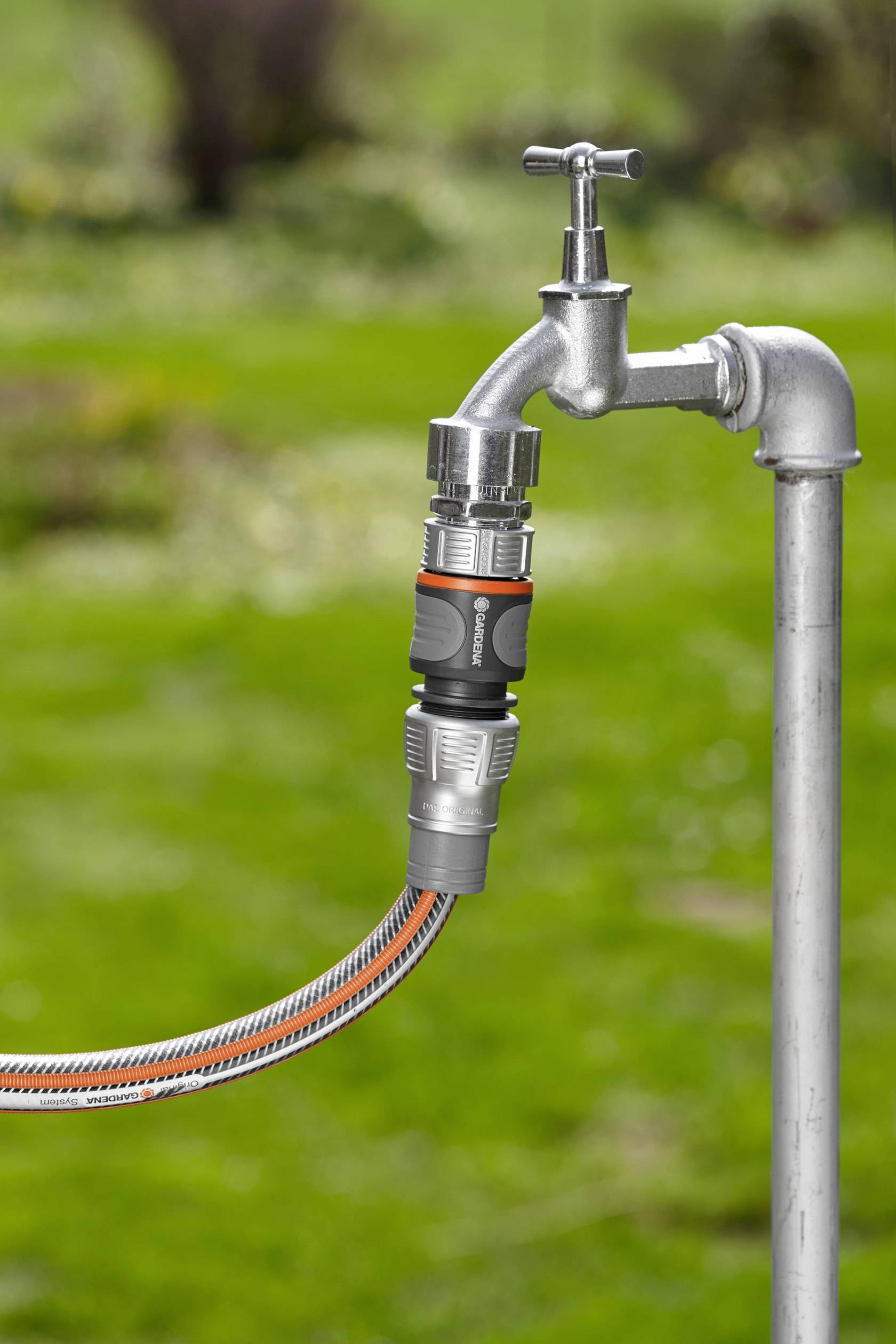 Ein Wasserhahn im Freien mit angeschlossenem Gartenschlauch, bereit zur Bewässerung eines Gartens im Hintergrund.