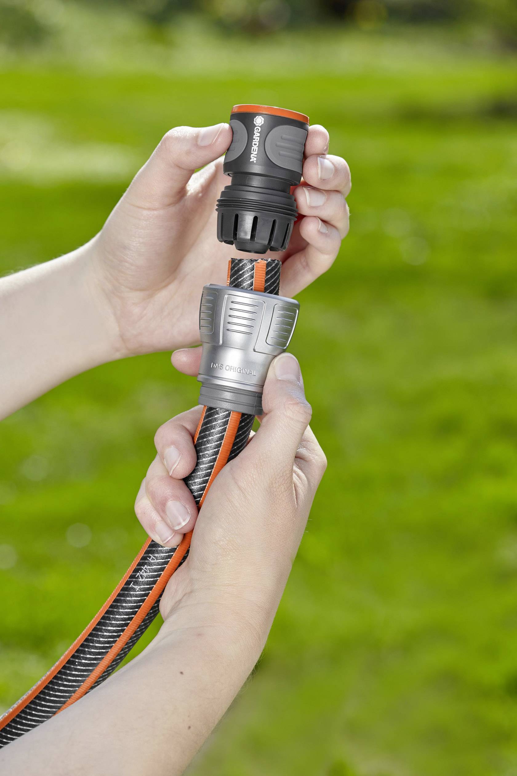 Zwei Hände verbinden ein Gartenschlauchstück mit einem Steckadapter auf einer grünen Wiese.