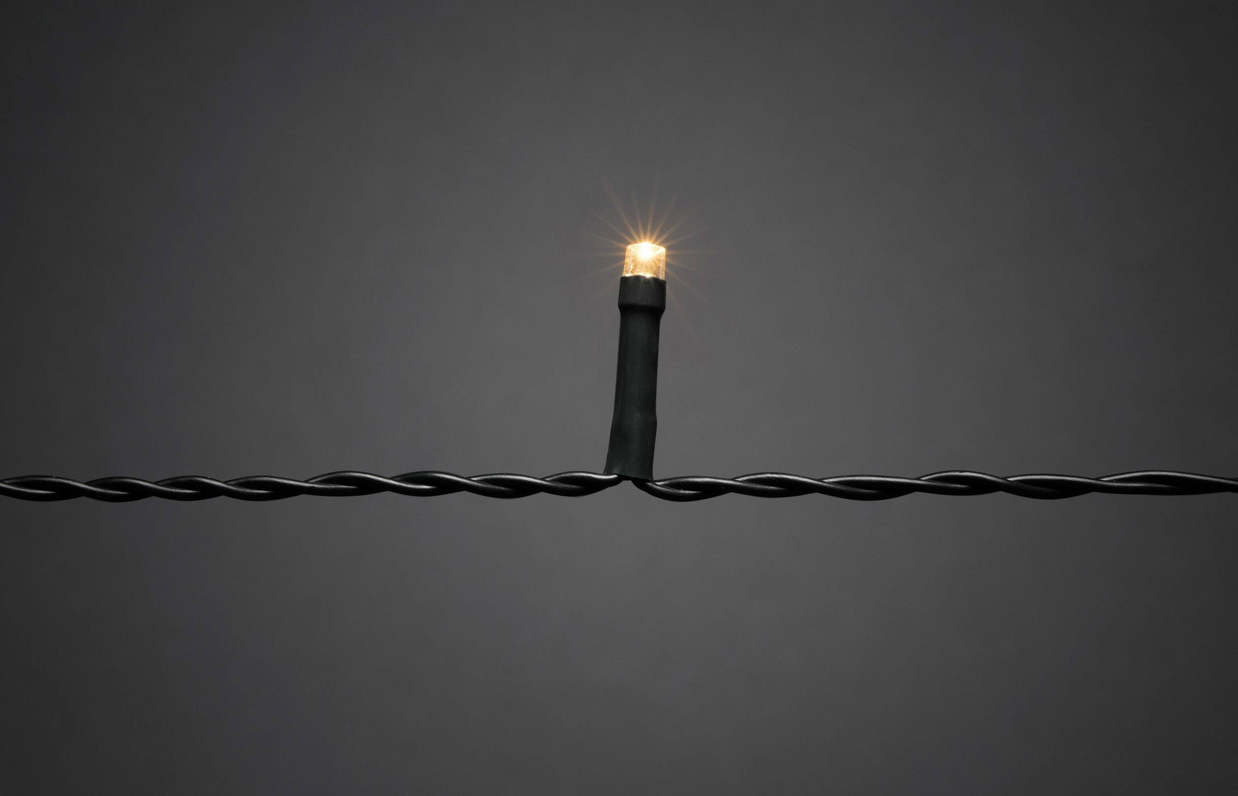 Eine einzelne, leuchtende Glühbirne auf einem verdrehten, schwarzen Draht vor grauem Hintergrund.