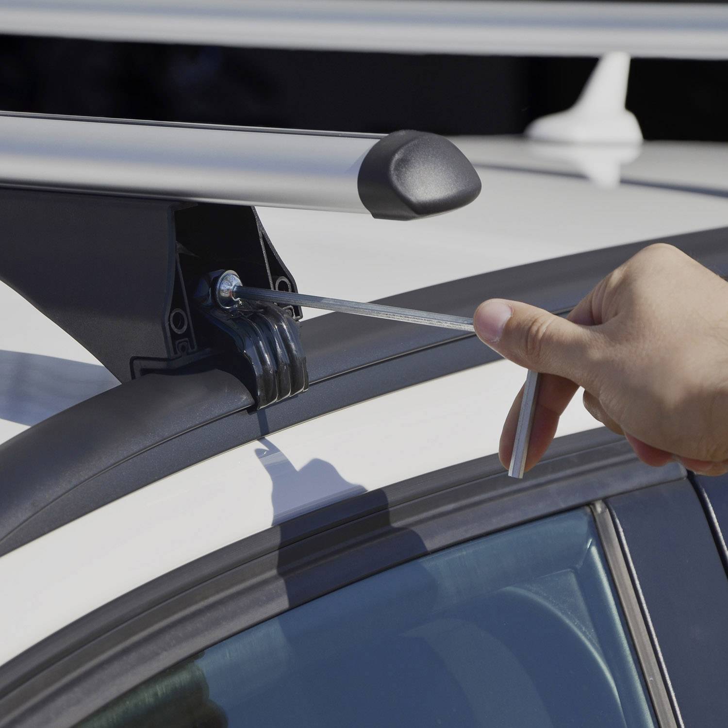 Eine Hand entfernt mit einem flachen Werkzeug eine Schraube von einem Dachträger auf einem Auto.