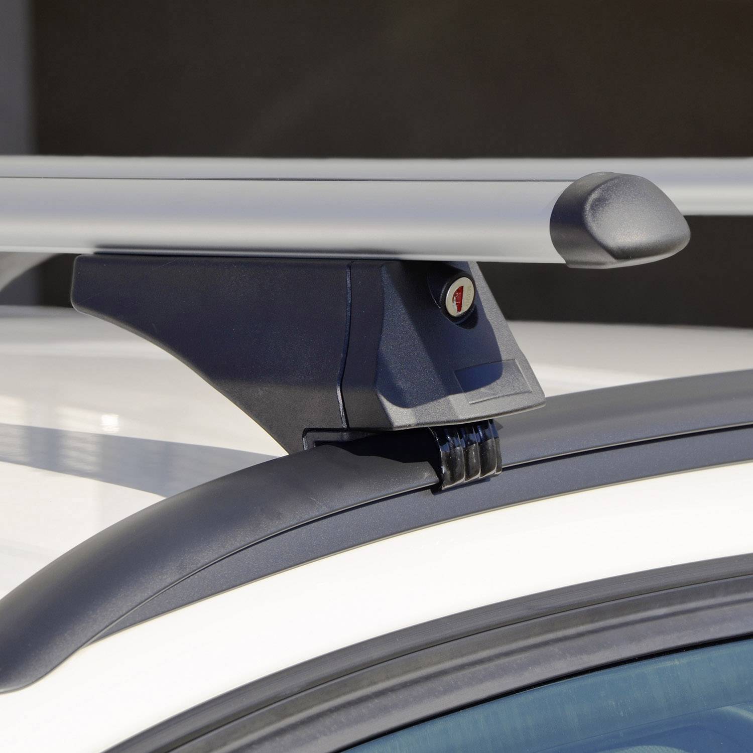 Eine Nahaufnahme eines Dachgepäckträgers auf einem weißen Auto. Der Träger hat eine Metallstange und eine Halterung.