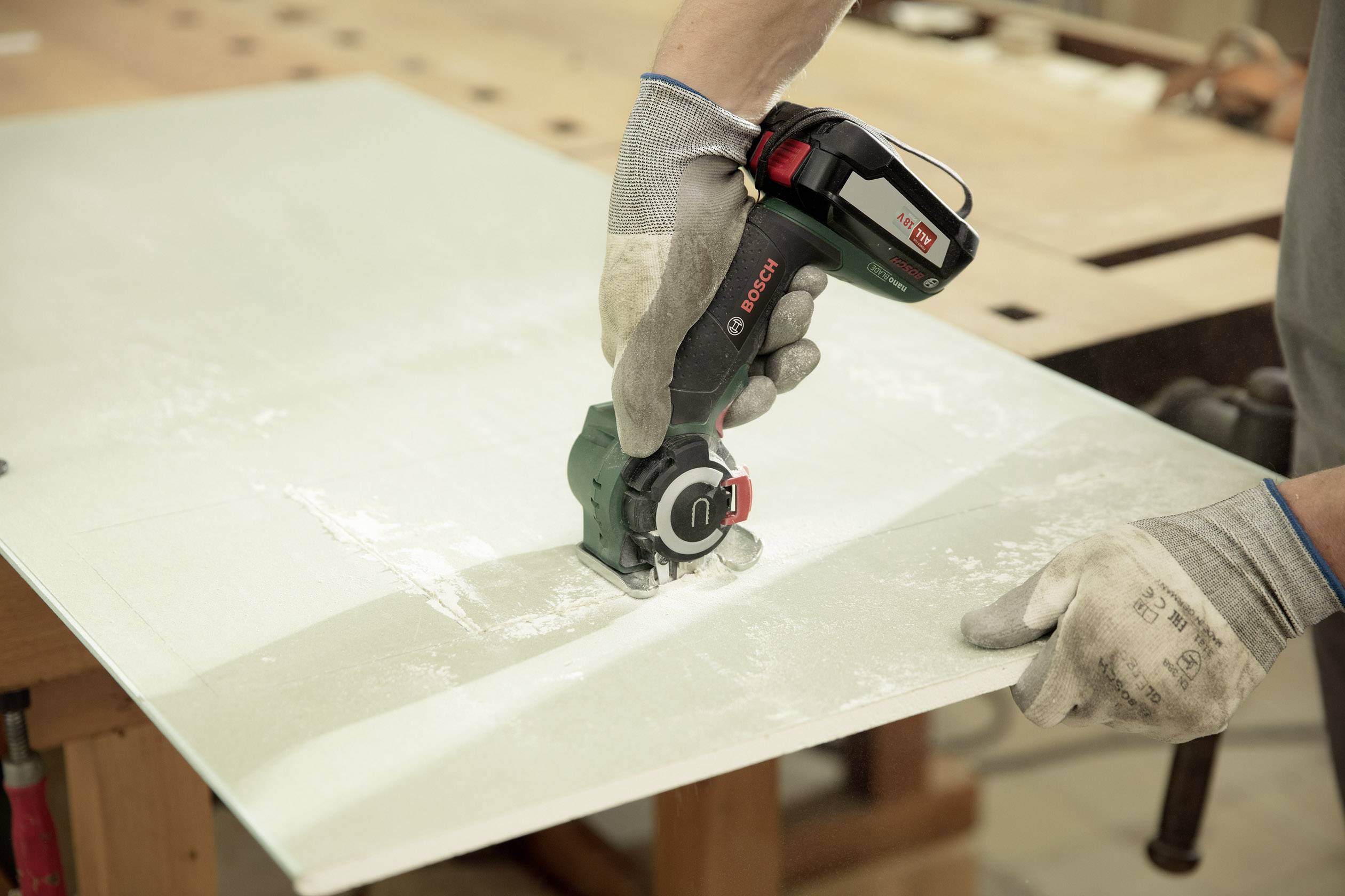 Eine Person schneidet mit einer Bosch-Schneidemaschine auf einem Tisch Glas. Die Person trägt Handschuhe zum Schutz.