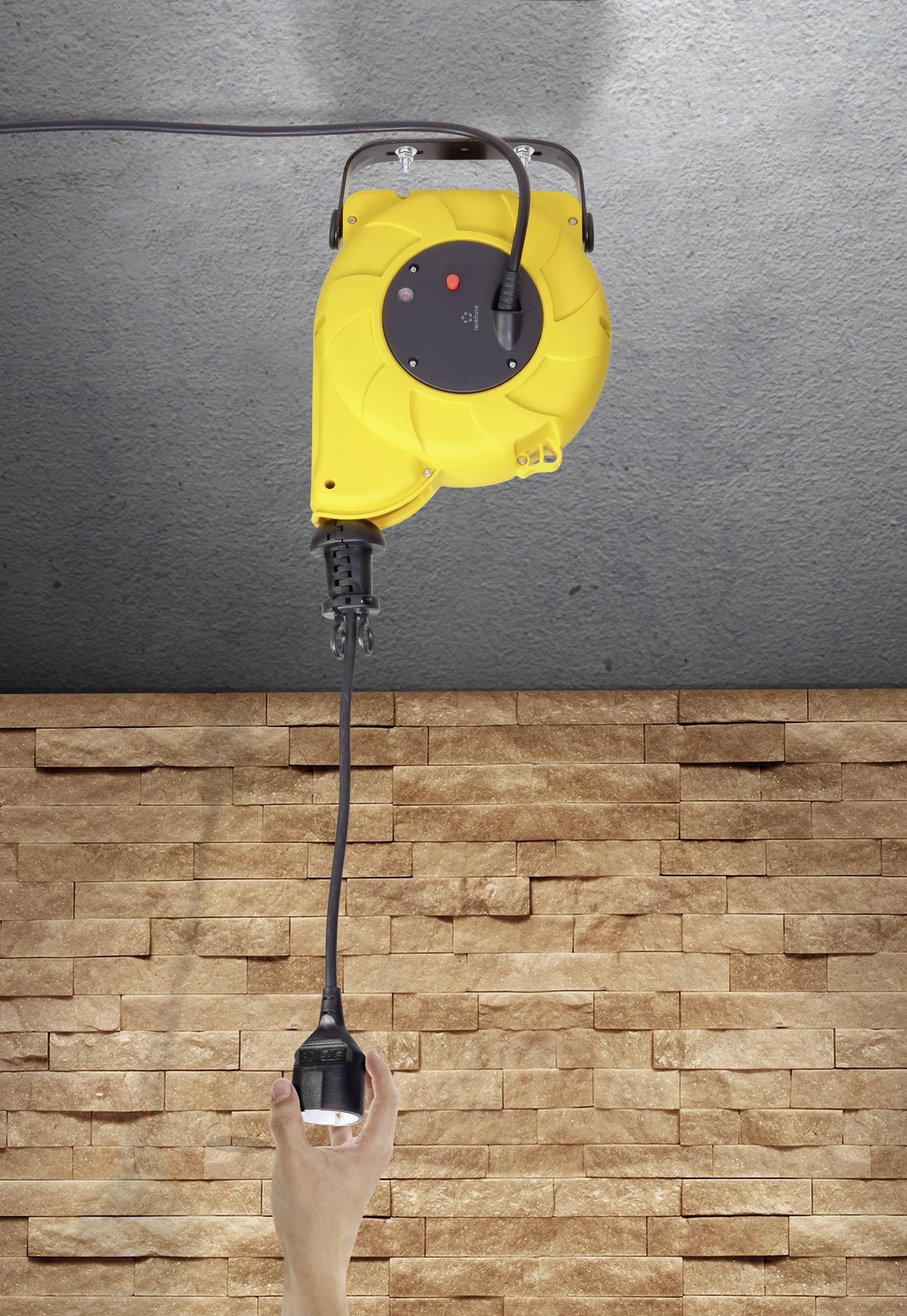 Gelbes, an der Decke montiertes Verlängerungskabel mit herunterhängendem Stecker; Hand greift nach Stecker vor Steinwandhintergrund.